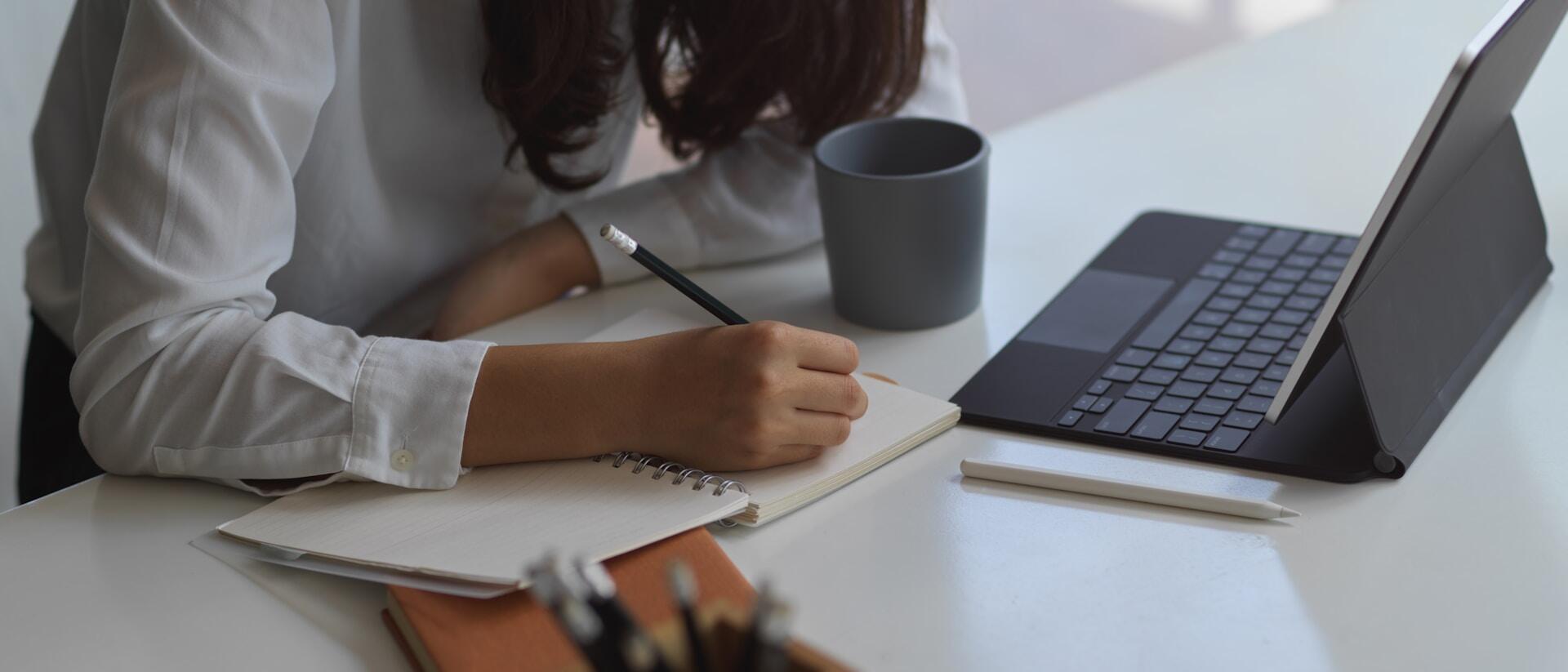 person taking notes in a notebook while looking at a computer screen