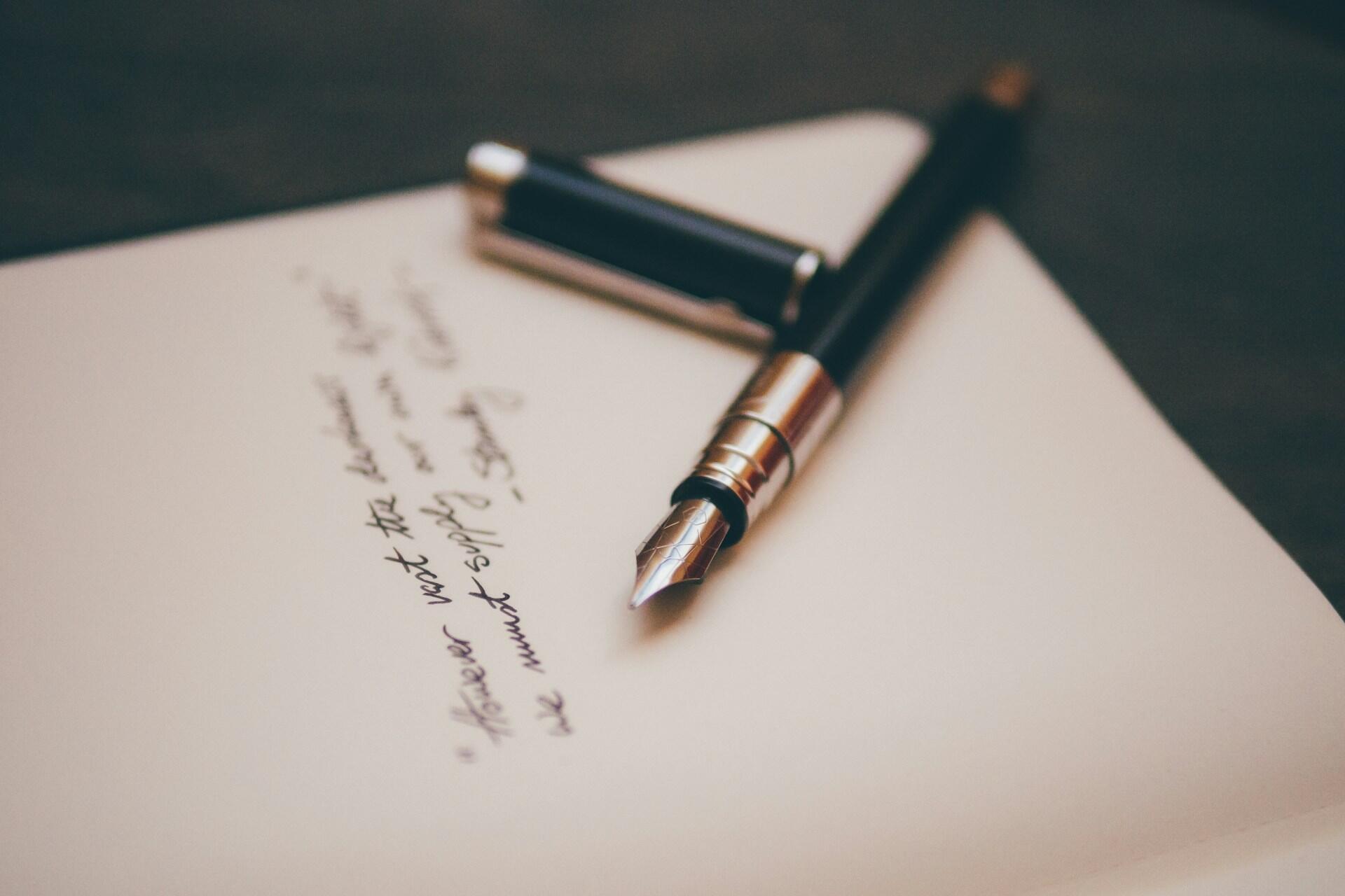 A pen resting on a notebook with poetry written in cursive..