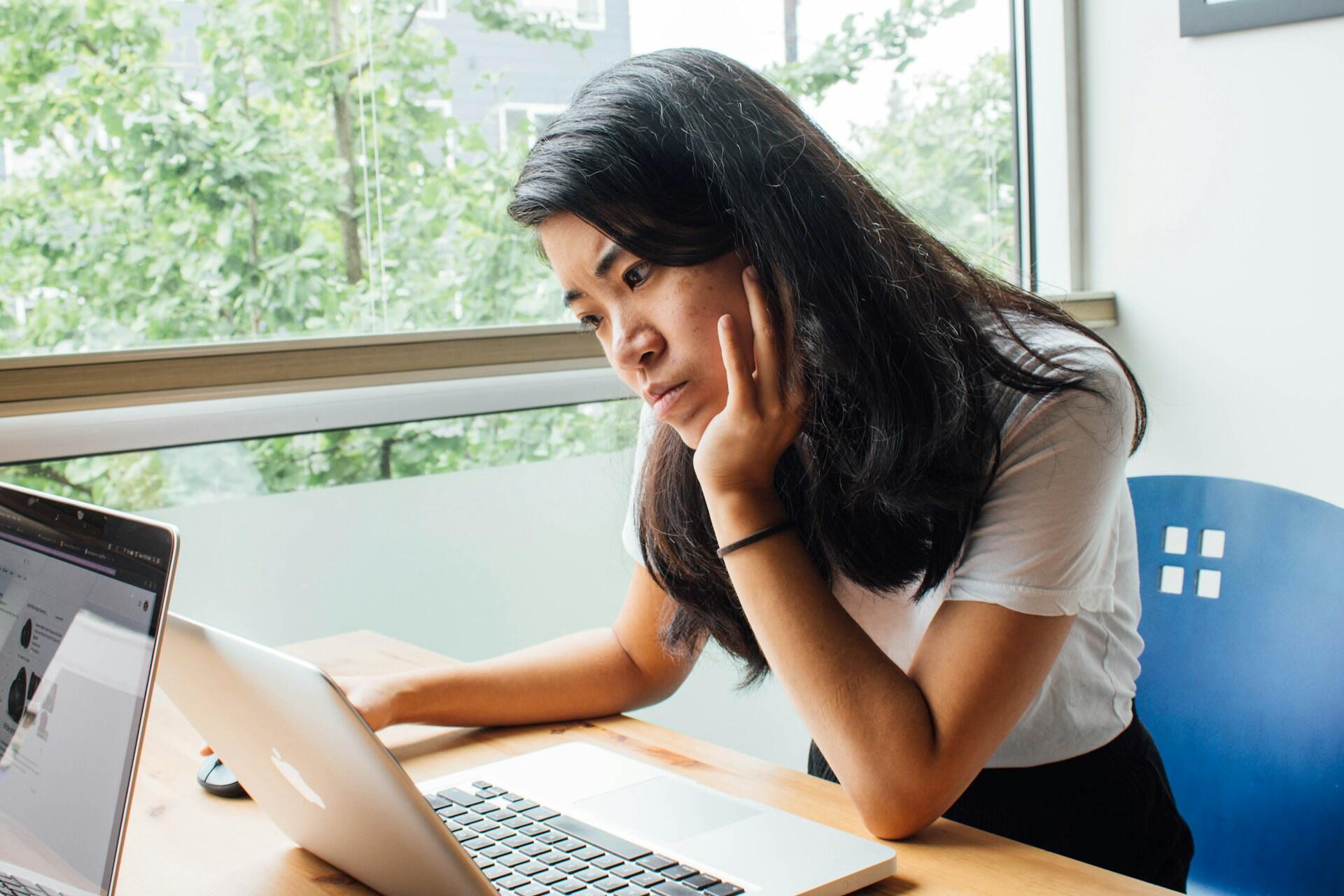 A girl resting her head on her hand while looking at her computer.