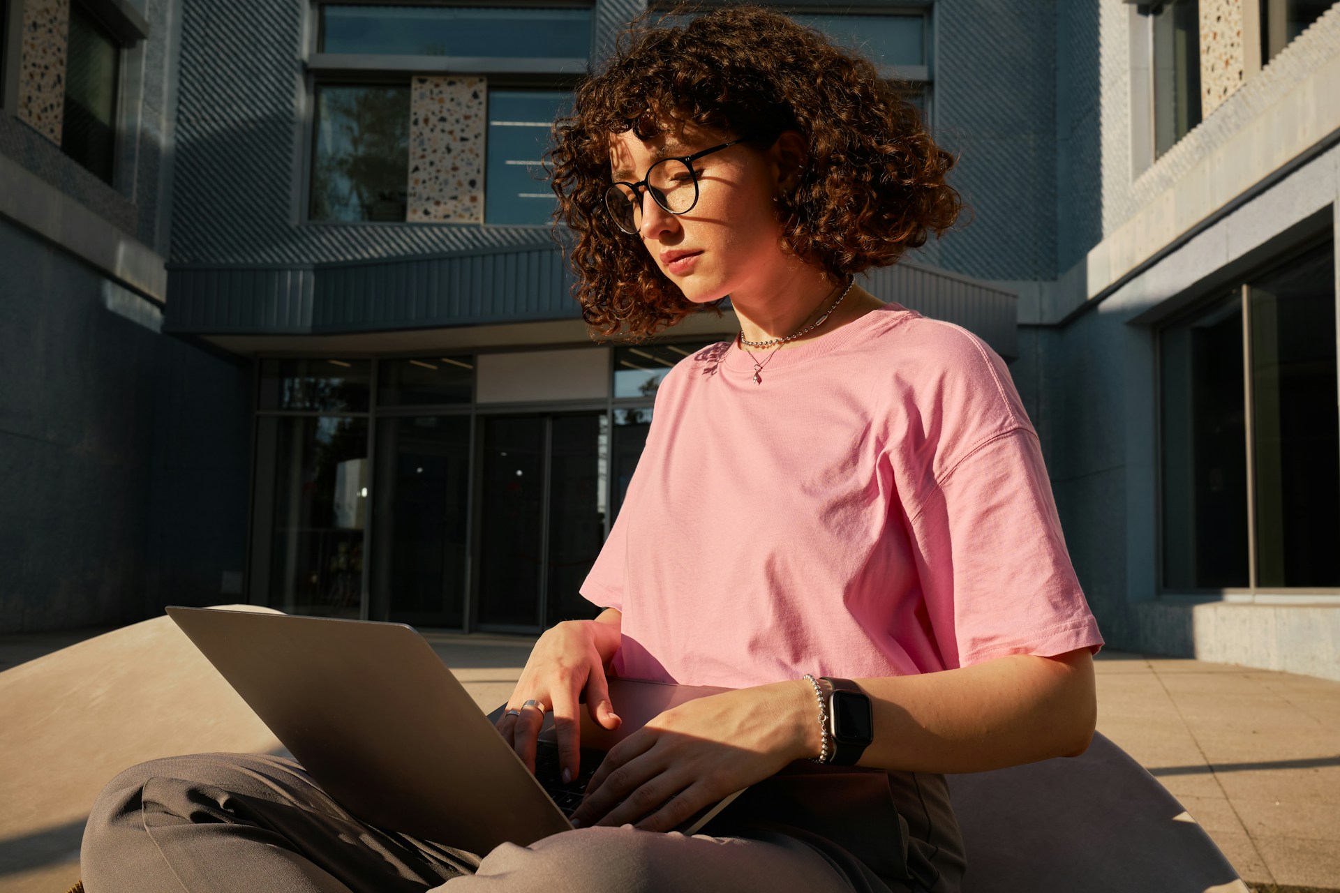 A girl in a pink shirt and glasses typing on a computer.