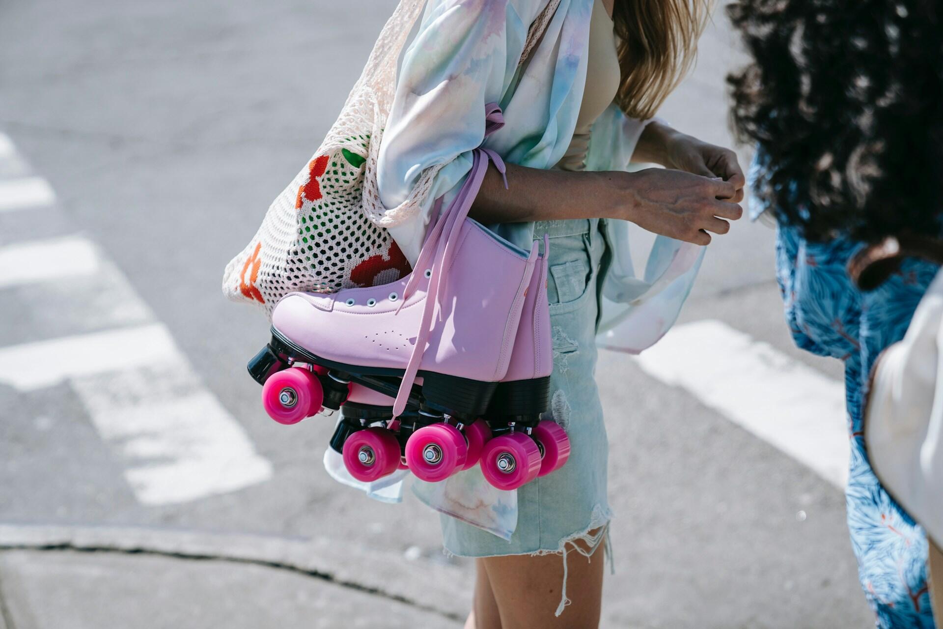 Person carrying pink quad roller skates over one shoulder