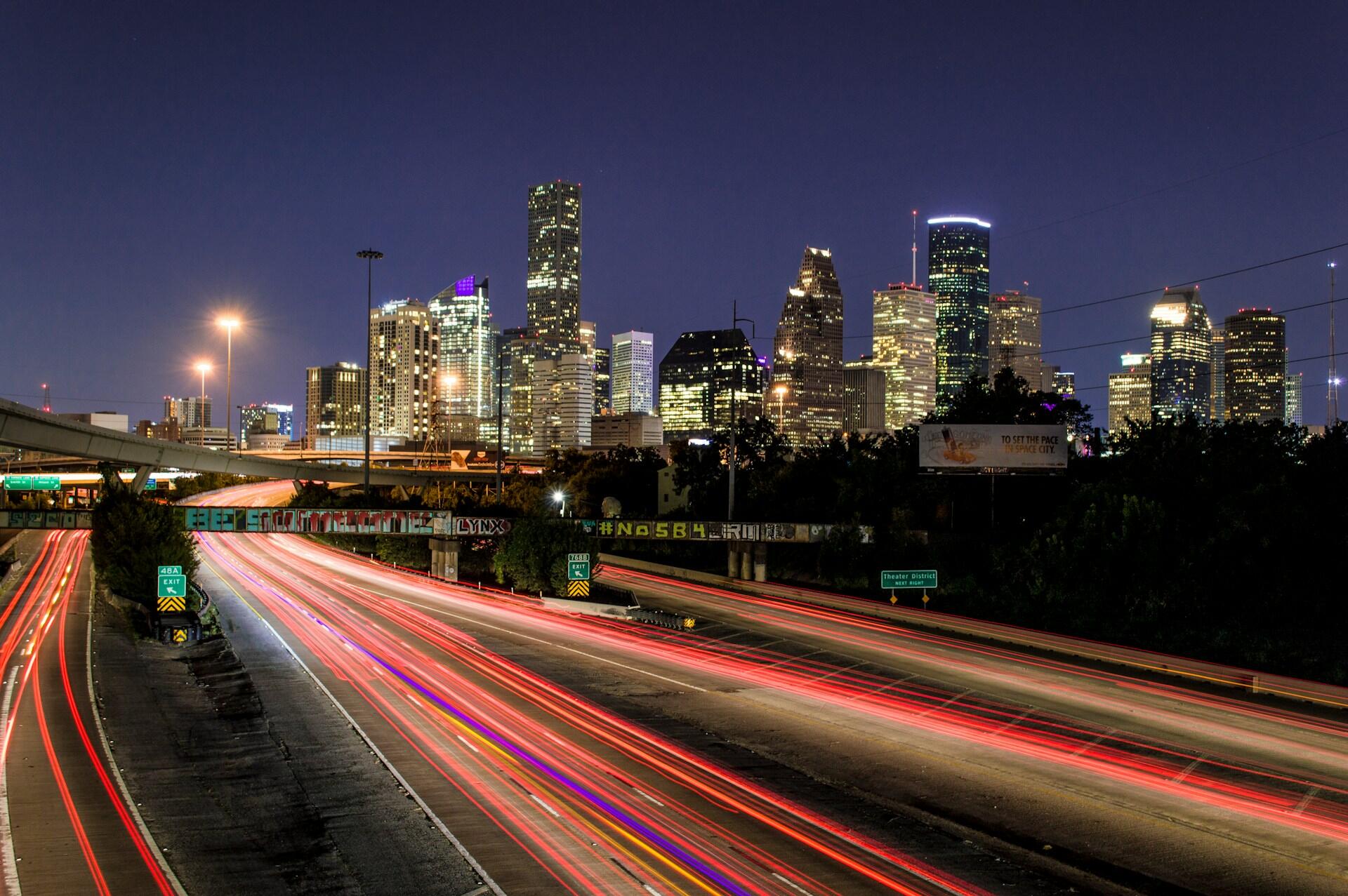 Houston skyline illuminated at night above a highway with light trails