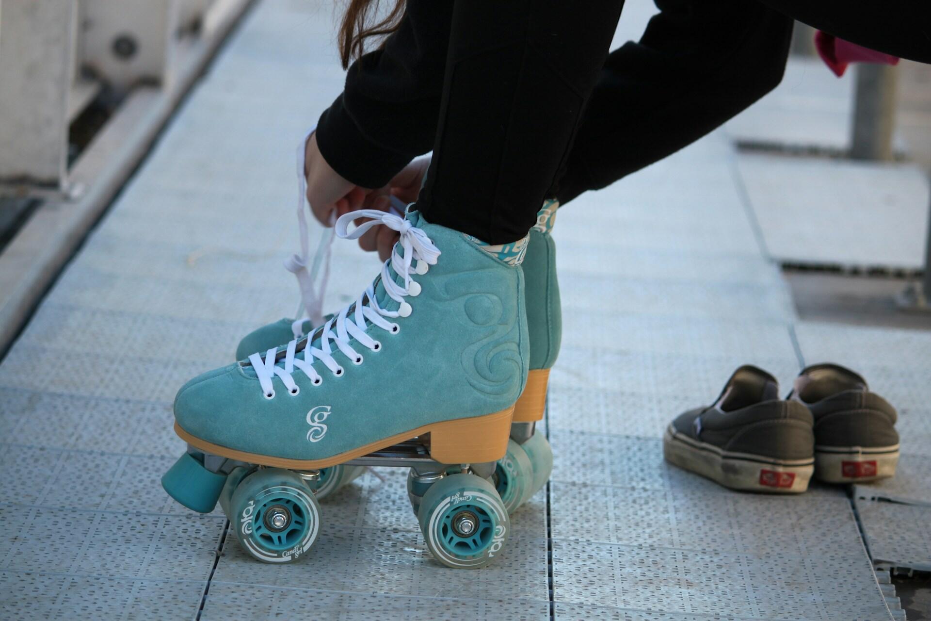 Person lacing turquoise roller skates beside a pair of shoes