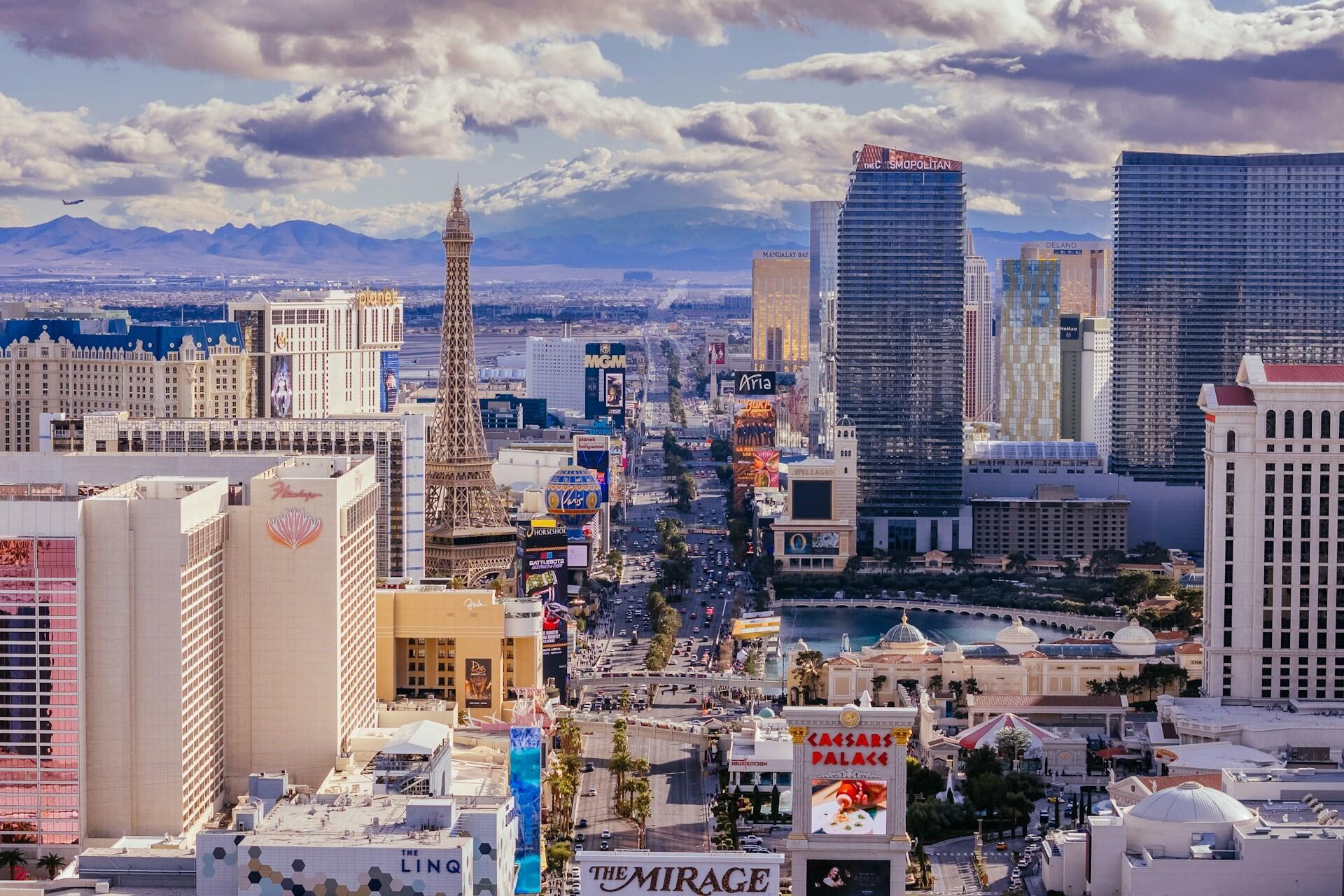 Daytime aerial view of the Las Vegas Strip with hotels, the Eiffel Tower replica, and mountains