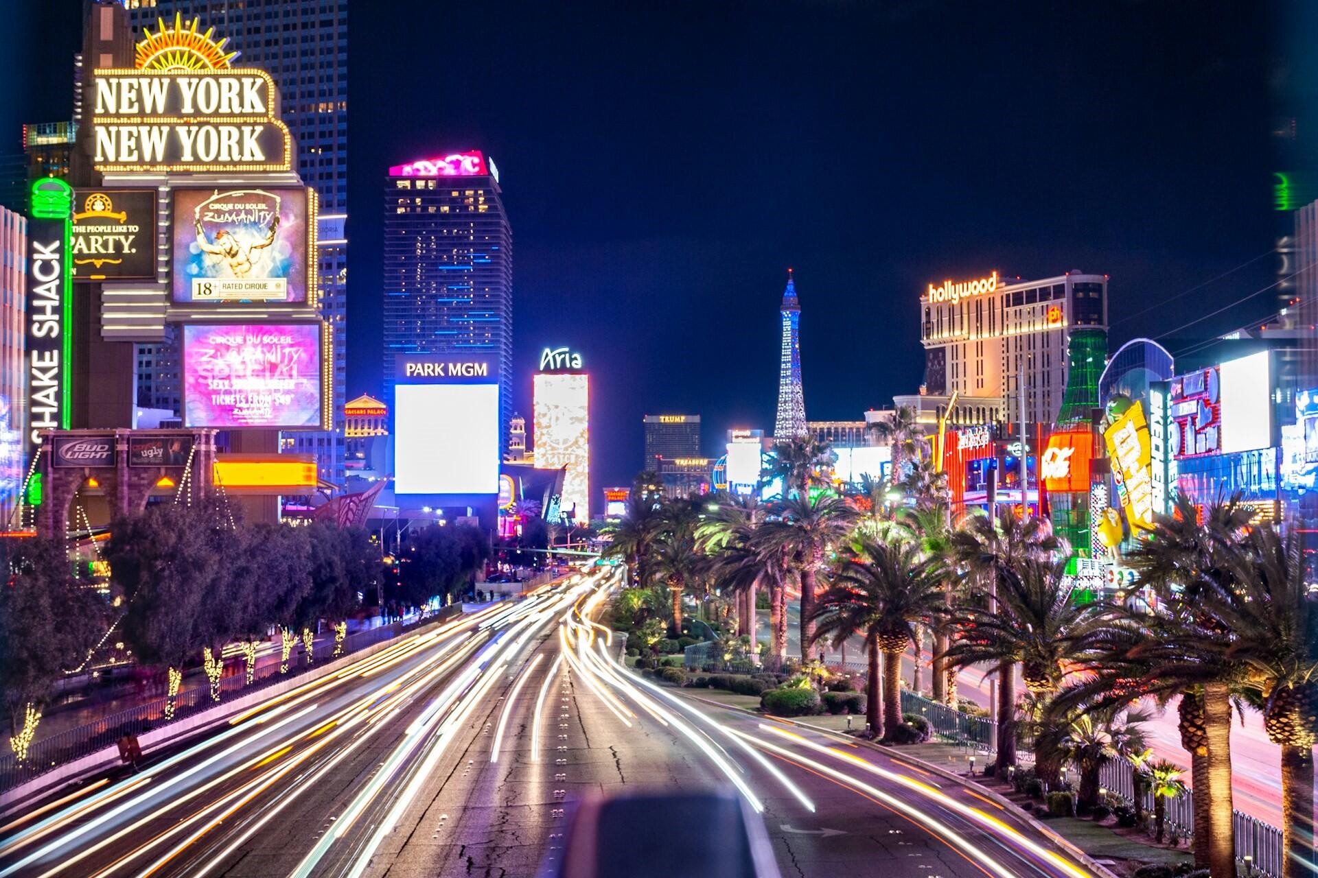 Las Vegas Strip at night with illuminated hotels, signs, palm trees, and traffic light trails