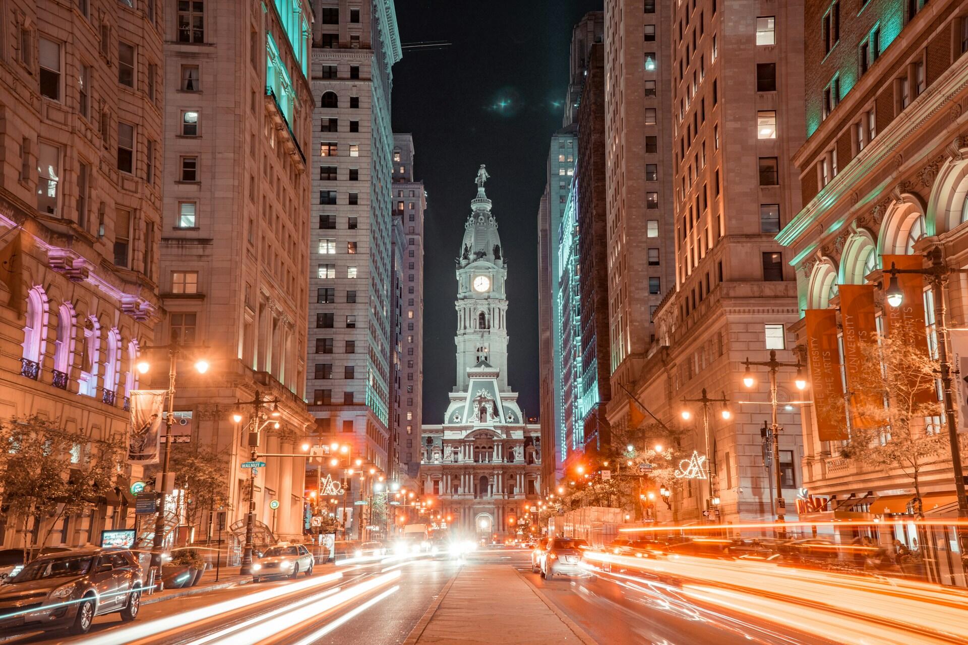 Philadelphia City Hall illuminated at night between downtown buildings