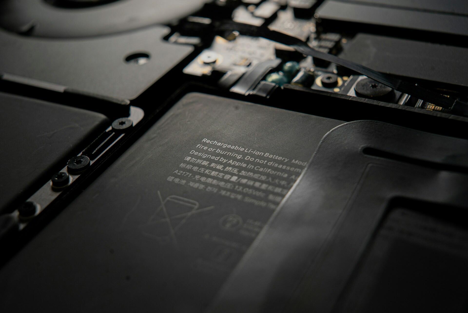 Close-up of an Apple lithium-ion battery, showing warning labels and internal circuit components in a sleek, black design.