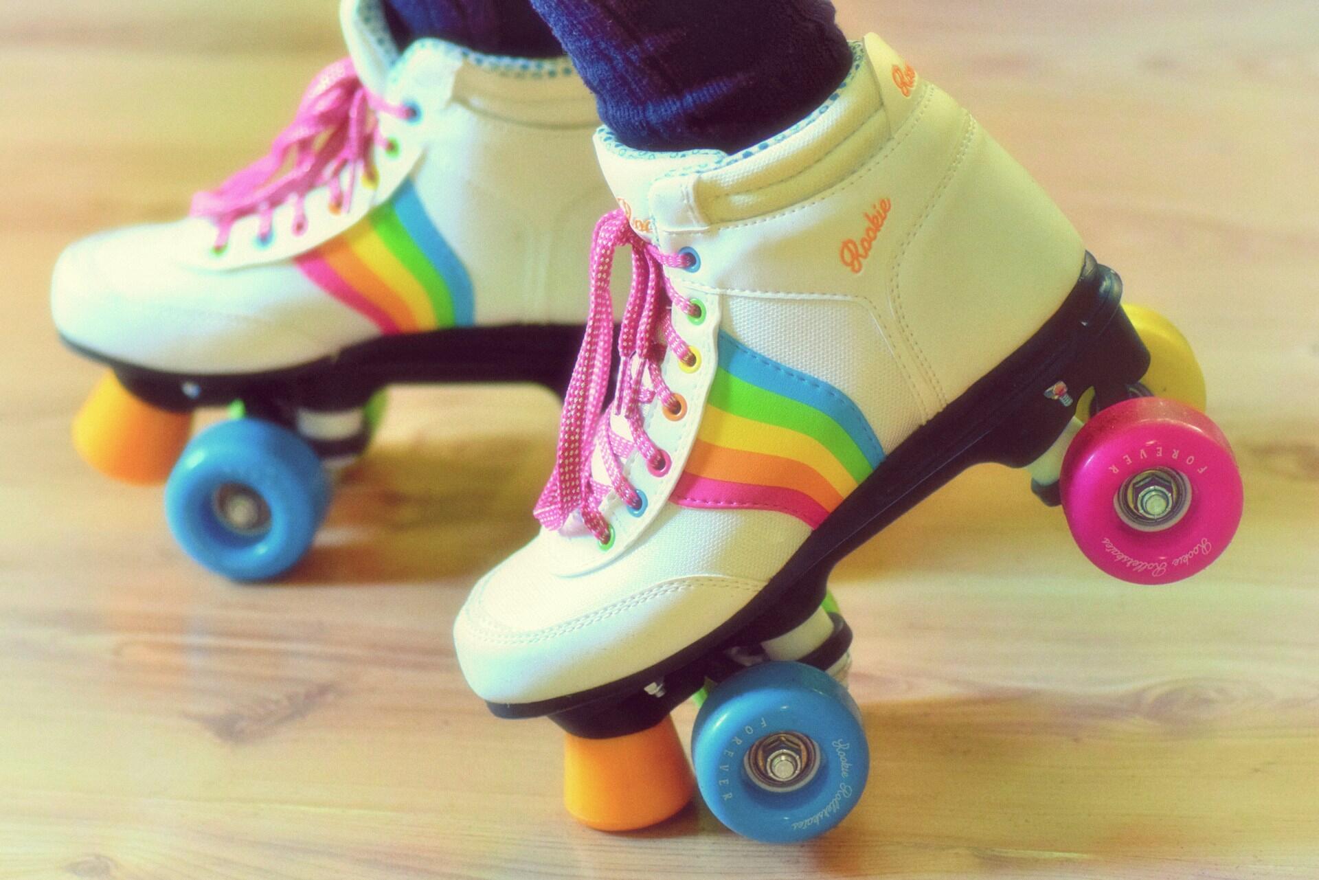White quad roller skates with rainbow stripes and colorful wheels on a wooden floor