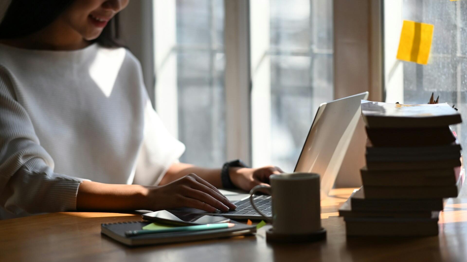person typing on a laptop computer with textbooks nearby on a desk