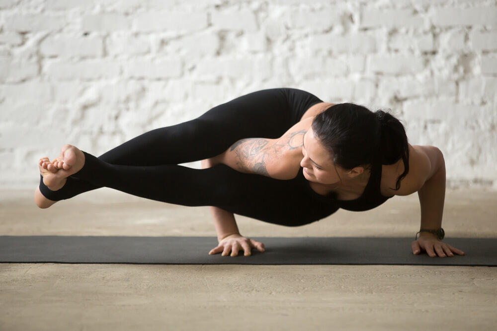 Woman balancing on her hands in eight angle pose, legs crossed at the ankles and extended to one side