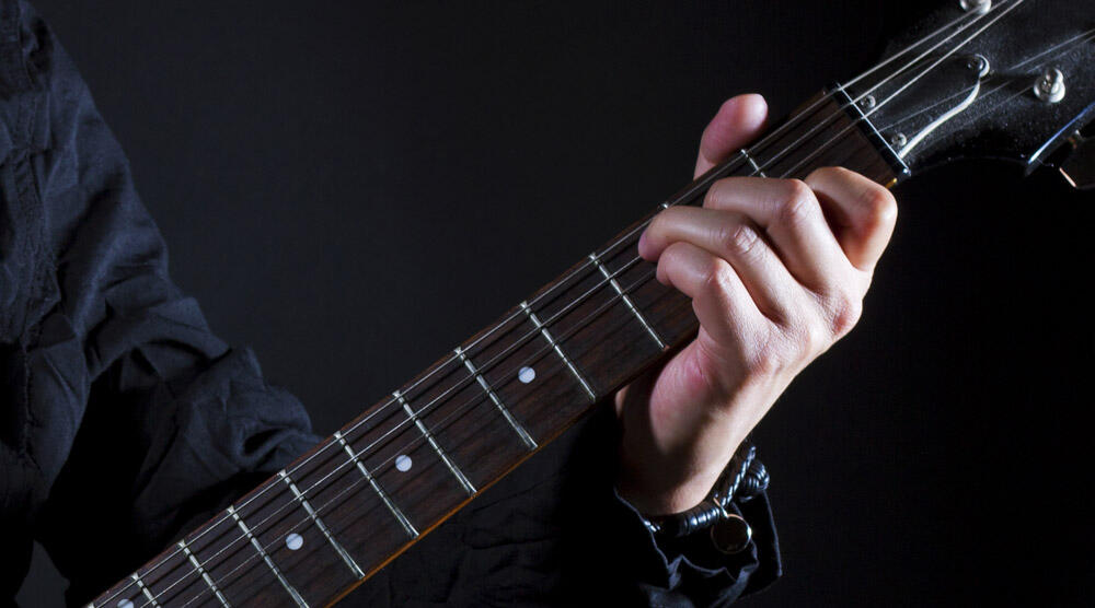 Guitarist’s fretting hand holding a power chord shape on the neck of a black electric guitar