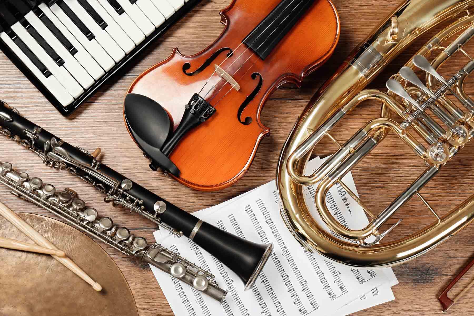 Keyboard, violin, clarinet, flute, horn, and drumsticks laid out on sheet music