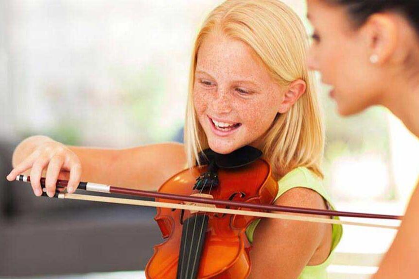 Smiling girl holding a violin and bow while her teacher watches