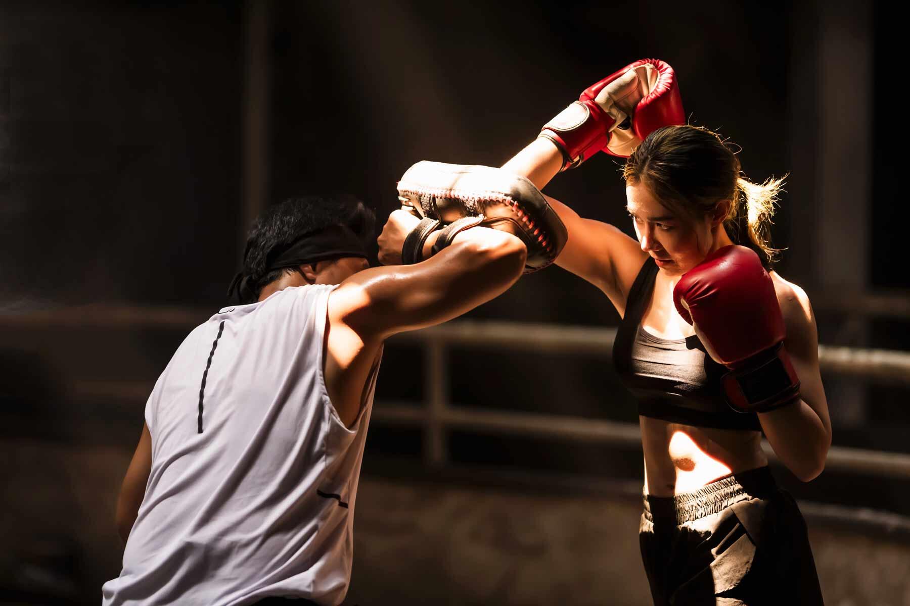 Woman in red gloves throwing a punch at a focus mitt held by her training partner