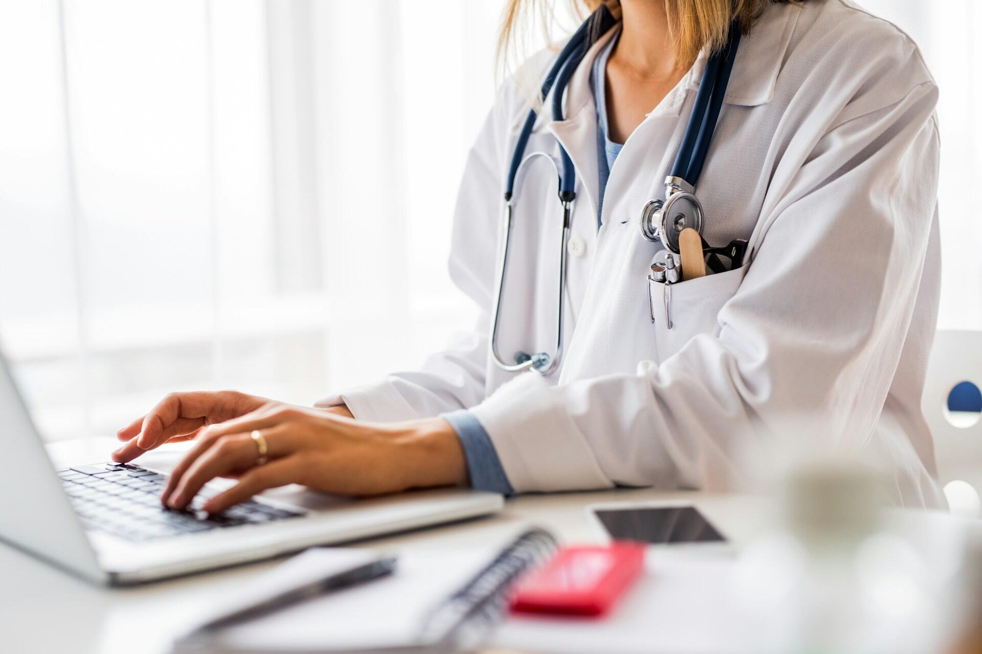 medical resident wearing a white coat and stethoscope typing on a computer