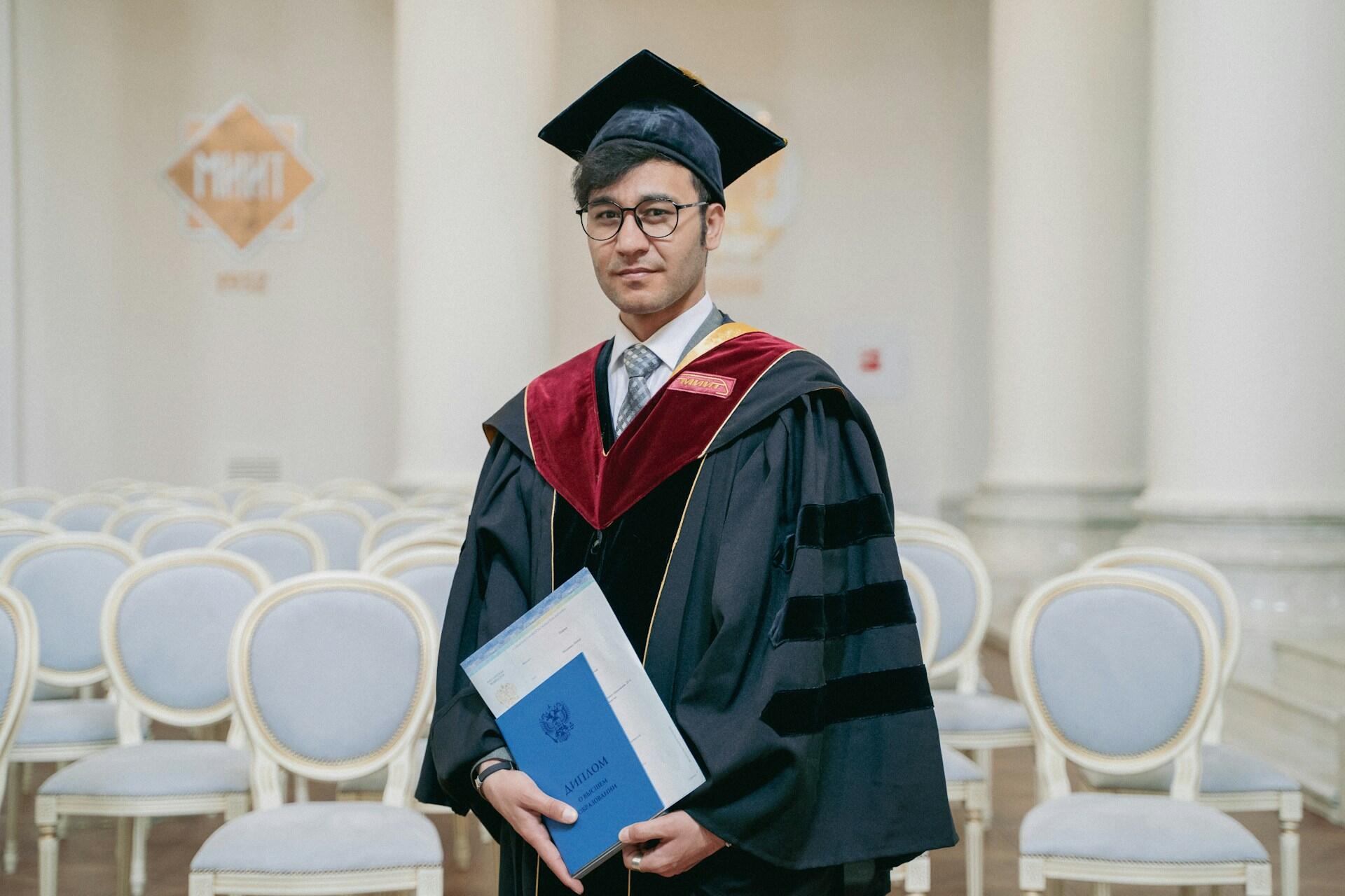 Doctorate graduate from medical school wearing distinctive gown with three velvet stripes and front panel, holding their diploma