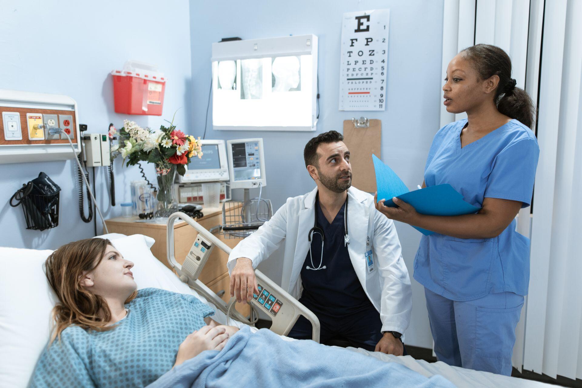 medical student reading patient's chart in an exam room with a Doctor supervising