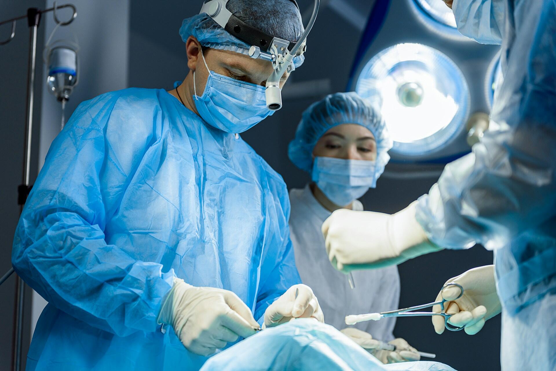 a surgeon with two attendings, each wearing full PPE, in an operating room, working on a patient