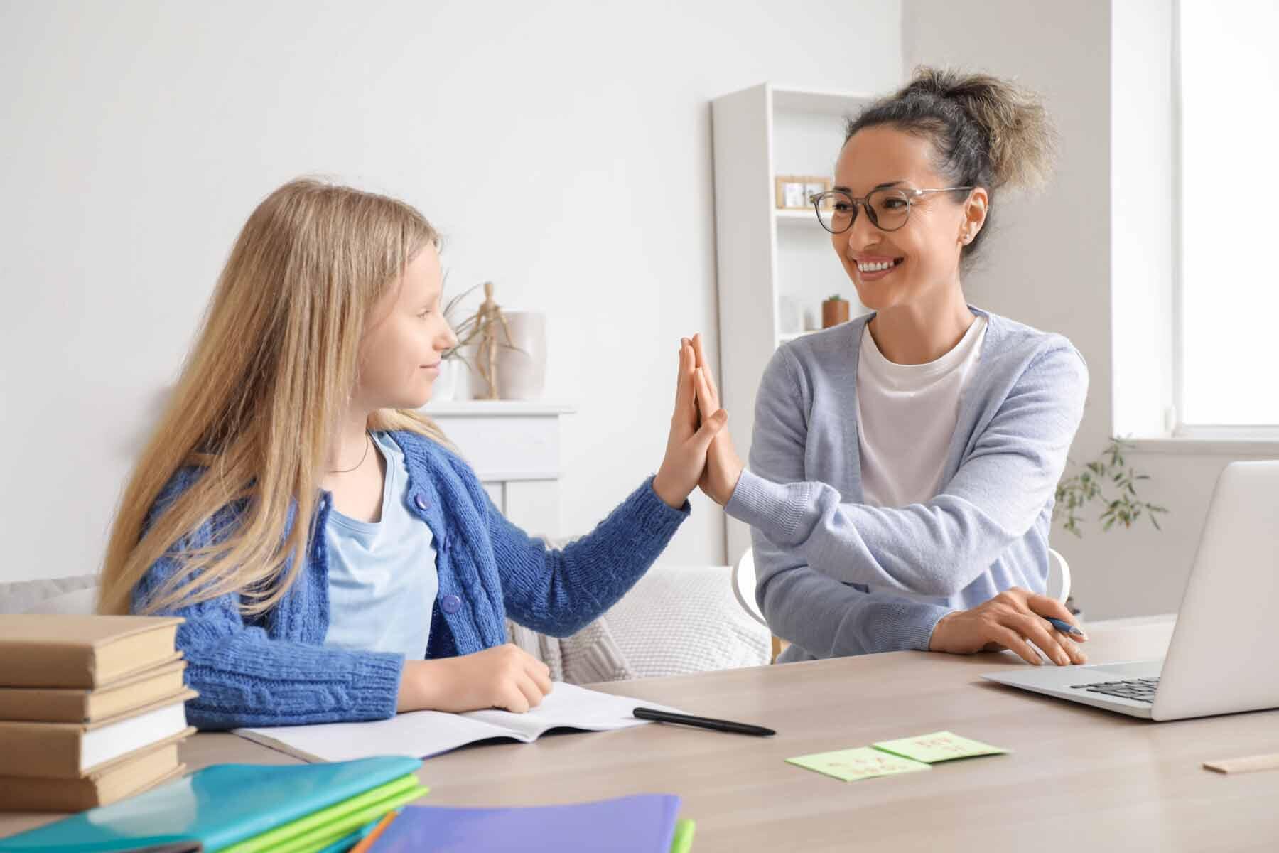 Tutor and student giving each other a high five at a desk with books and a laptop