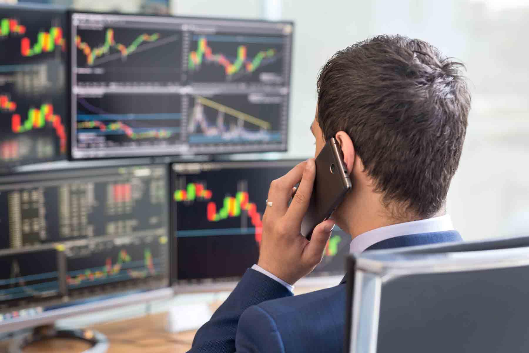 A financial broker viewing stock market activity while talking with a client on the phone