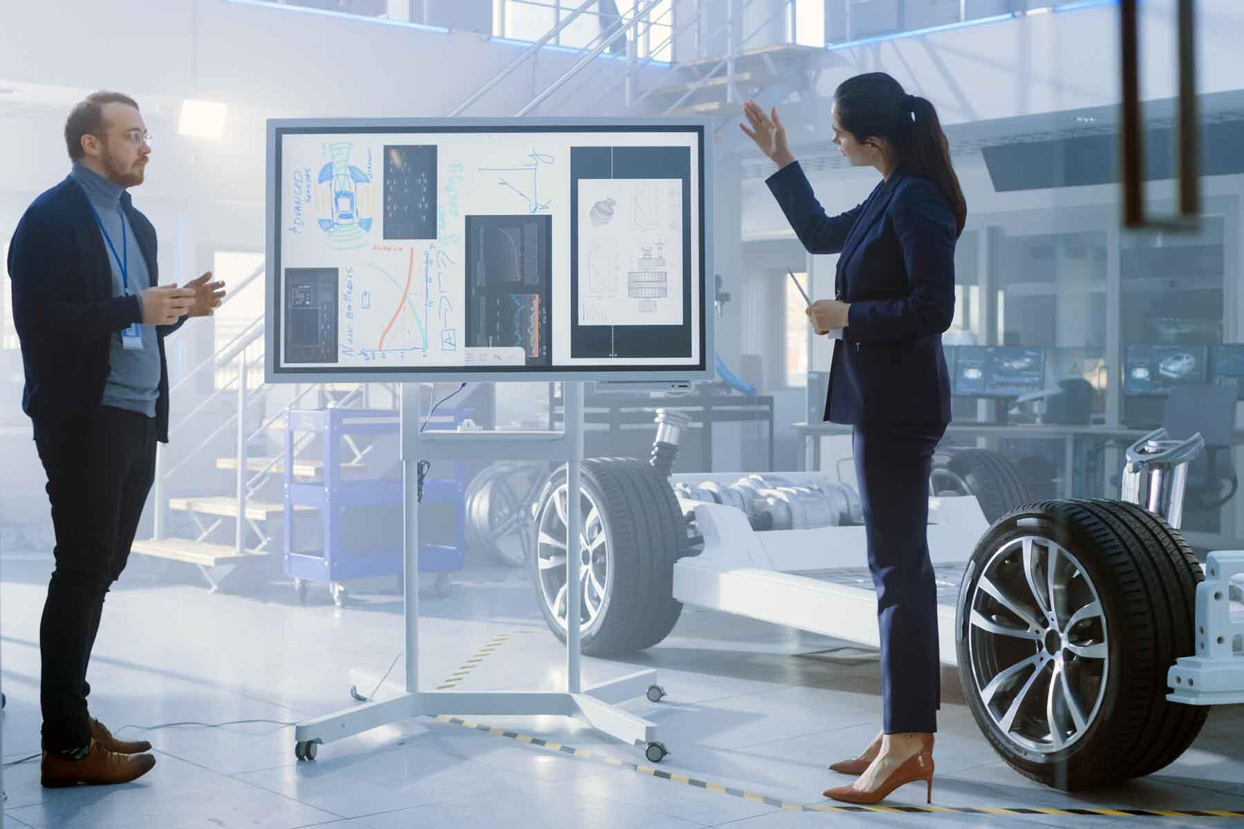 Two designers reviewing ideas on a smart board mounted on a floor stand.