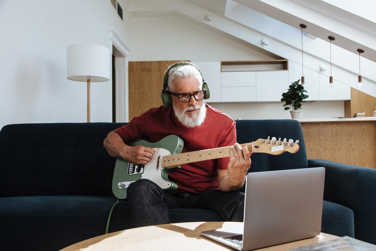 Hombre practicando tocar la guitarra, frente a la computadora.