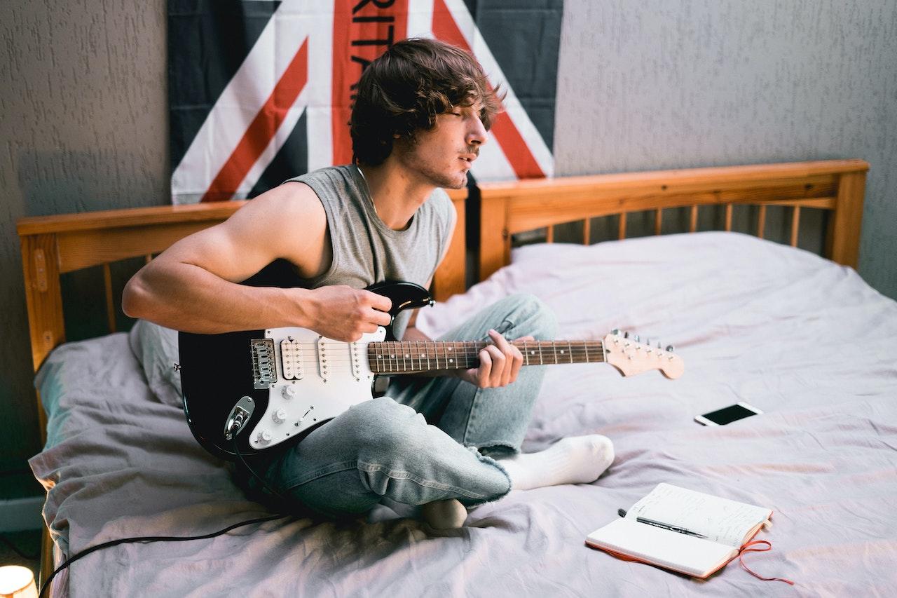Chico en la cama practicando tocar la guitarra