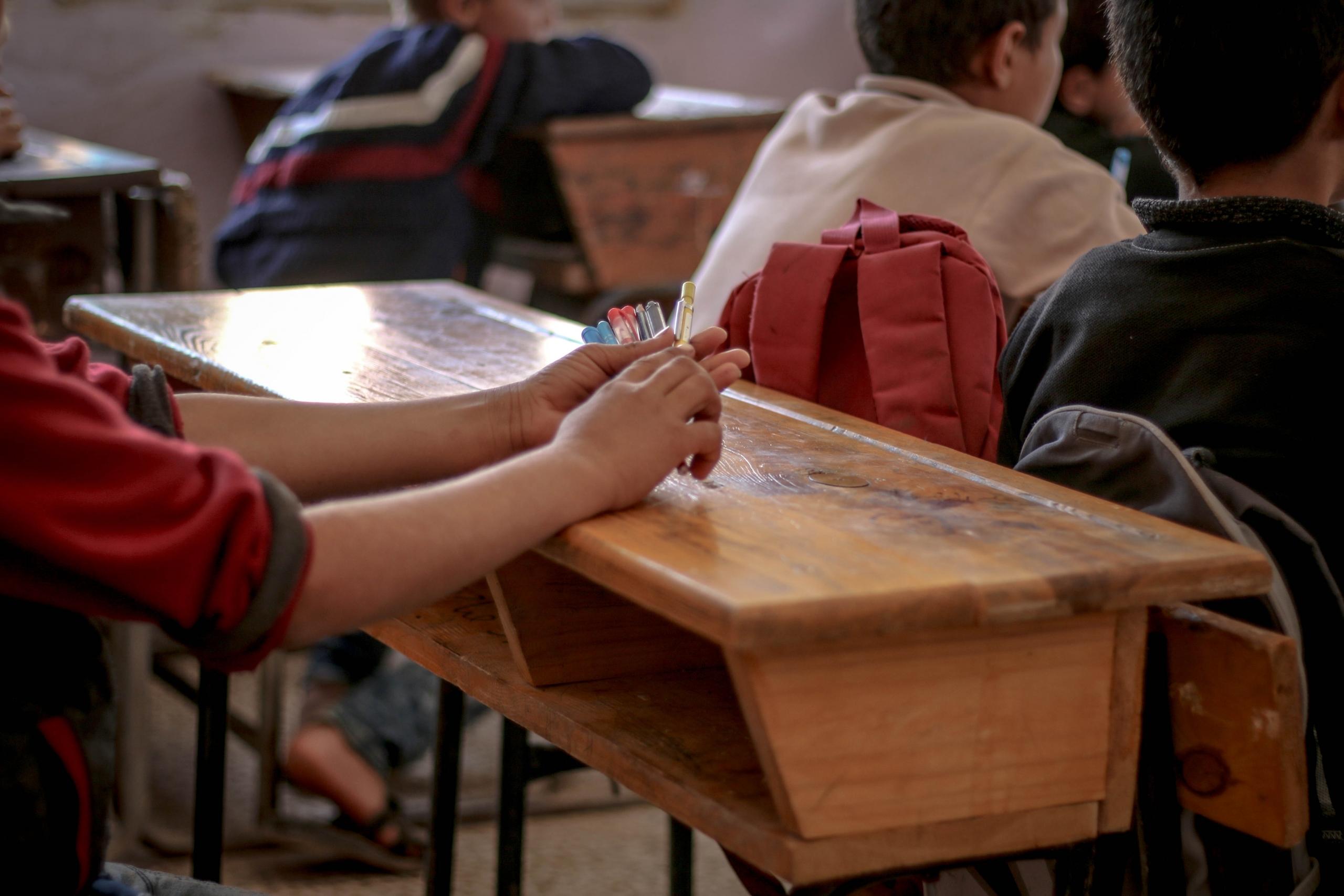 niño con fibrones sentado en un banco de una clase