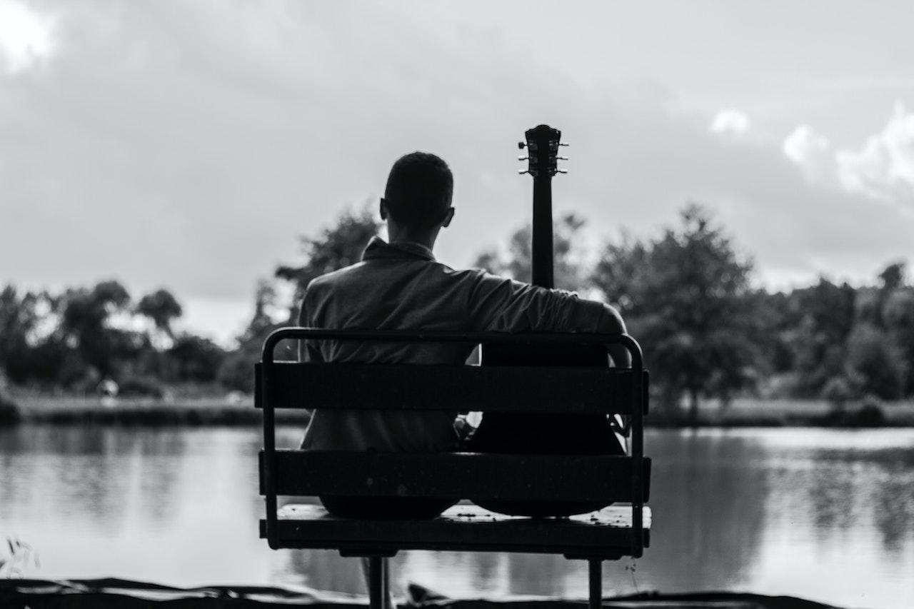 Hombre sentado, frente al rio, junto a su guitarra.