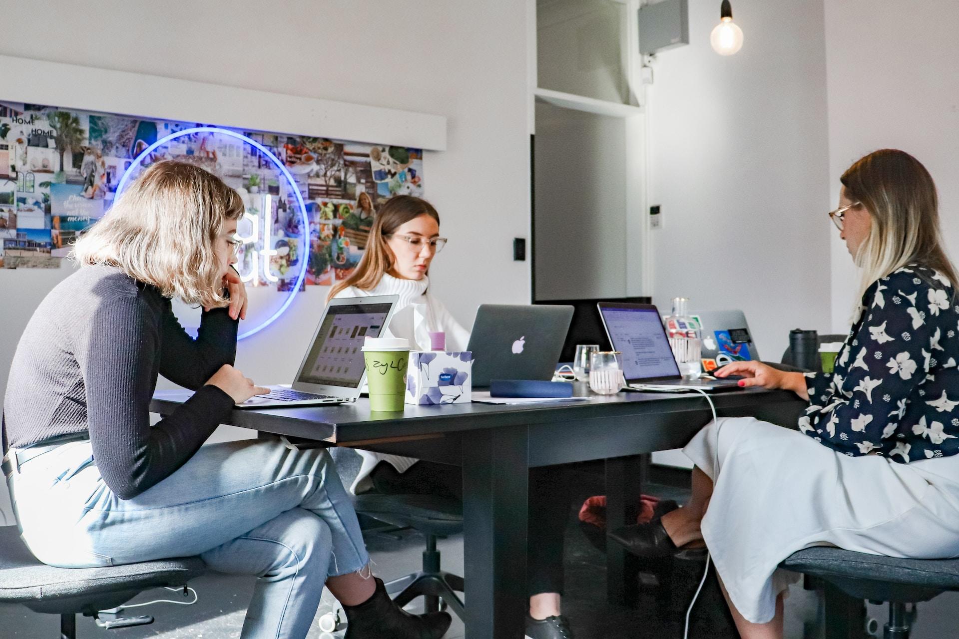 mujeres sentadas en una mesa con sus computadoras