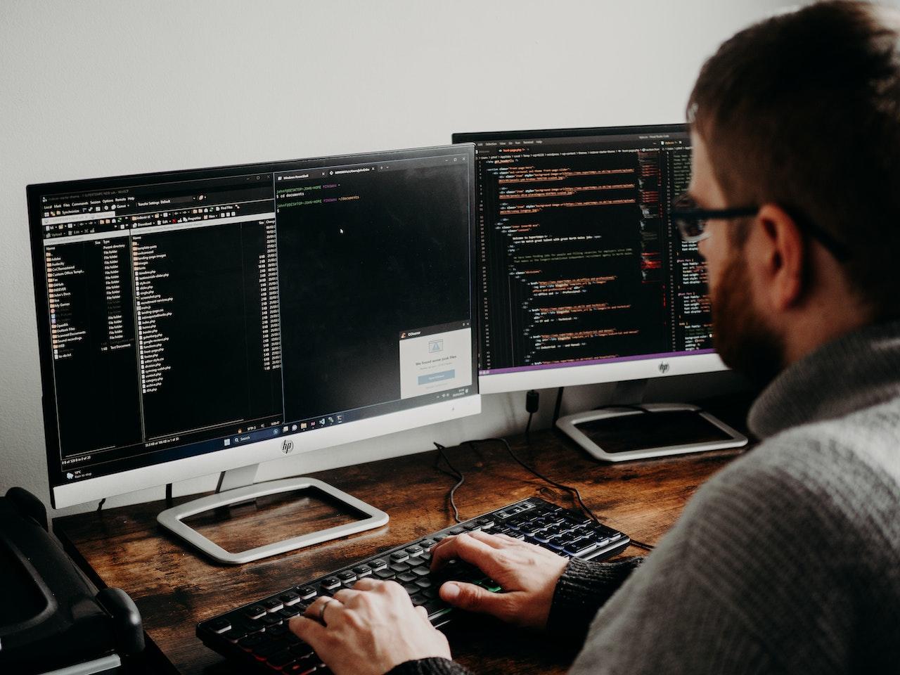 Persona frente a dos pantallas, utilizando lenguajes de programación