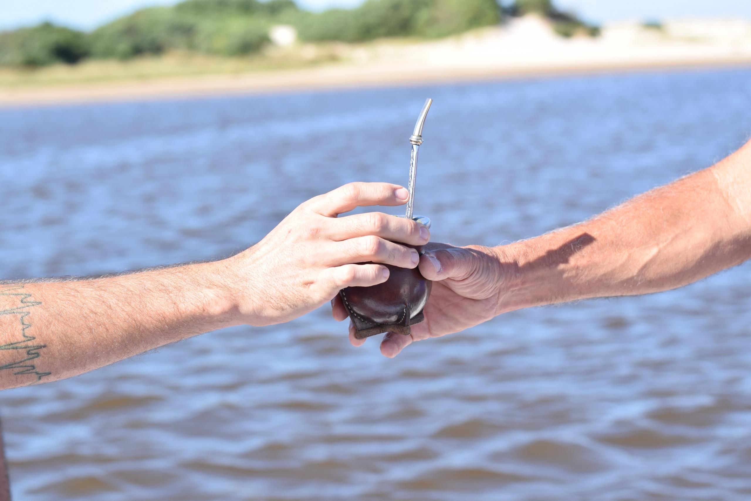 manos pasandose un mate al fernte de un rio