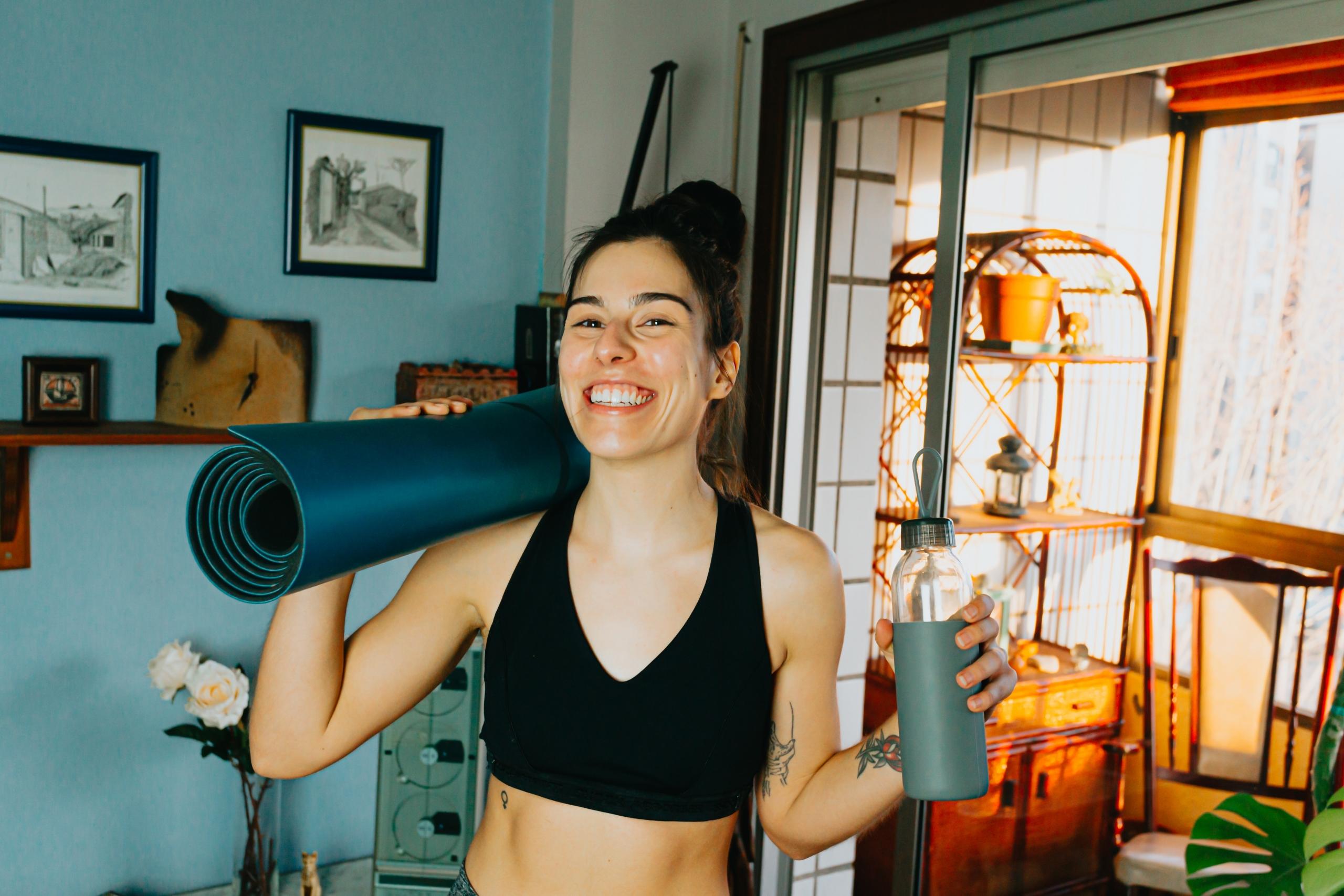 persona sonriendo sosteniendo una mat y una botella de agua