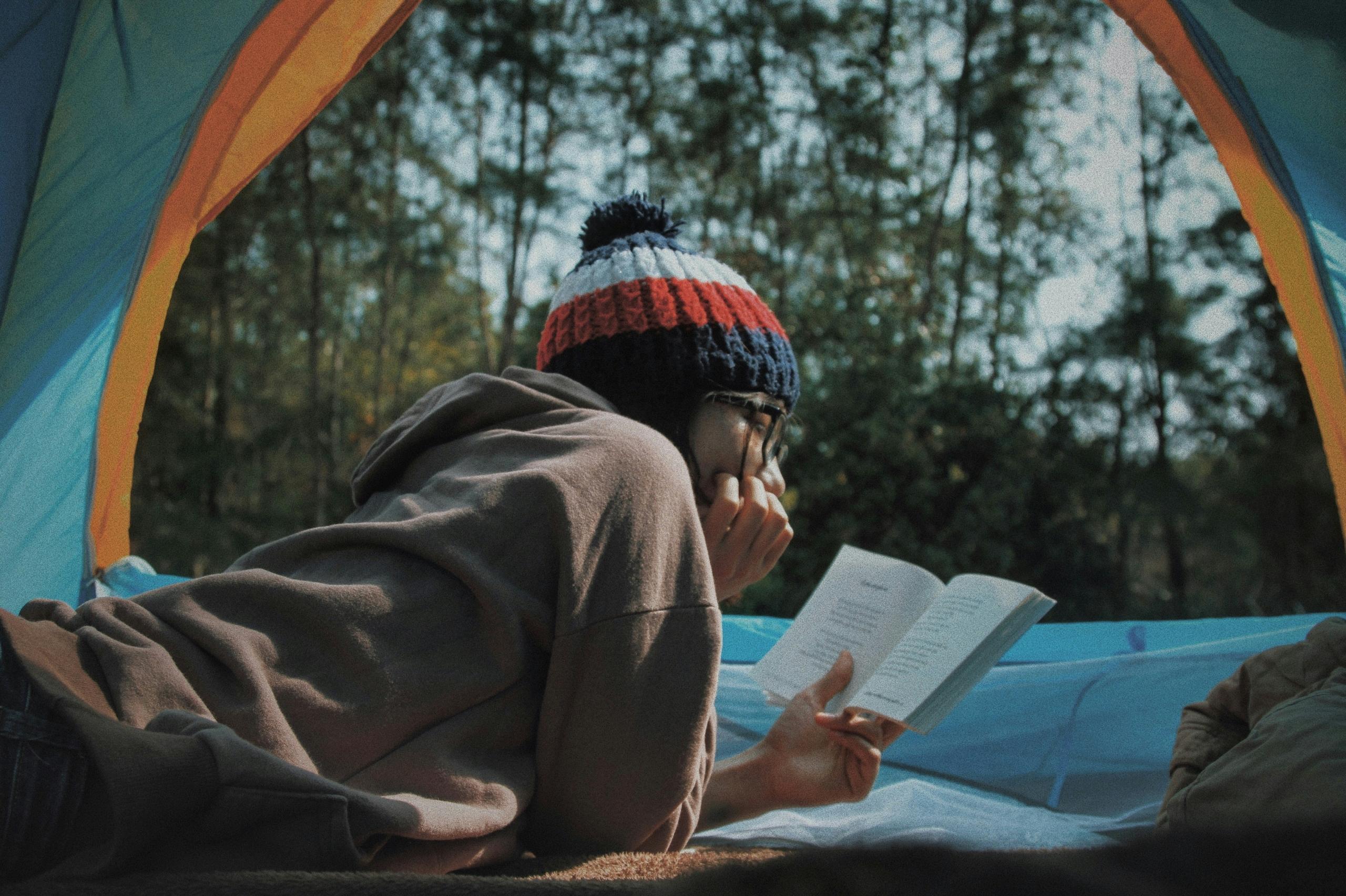 persona leyendo tirada dentro de una carpa, con un bosque de fondo