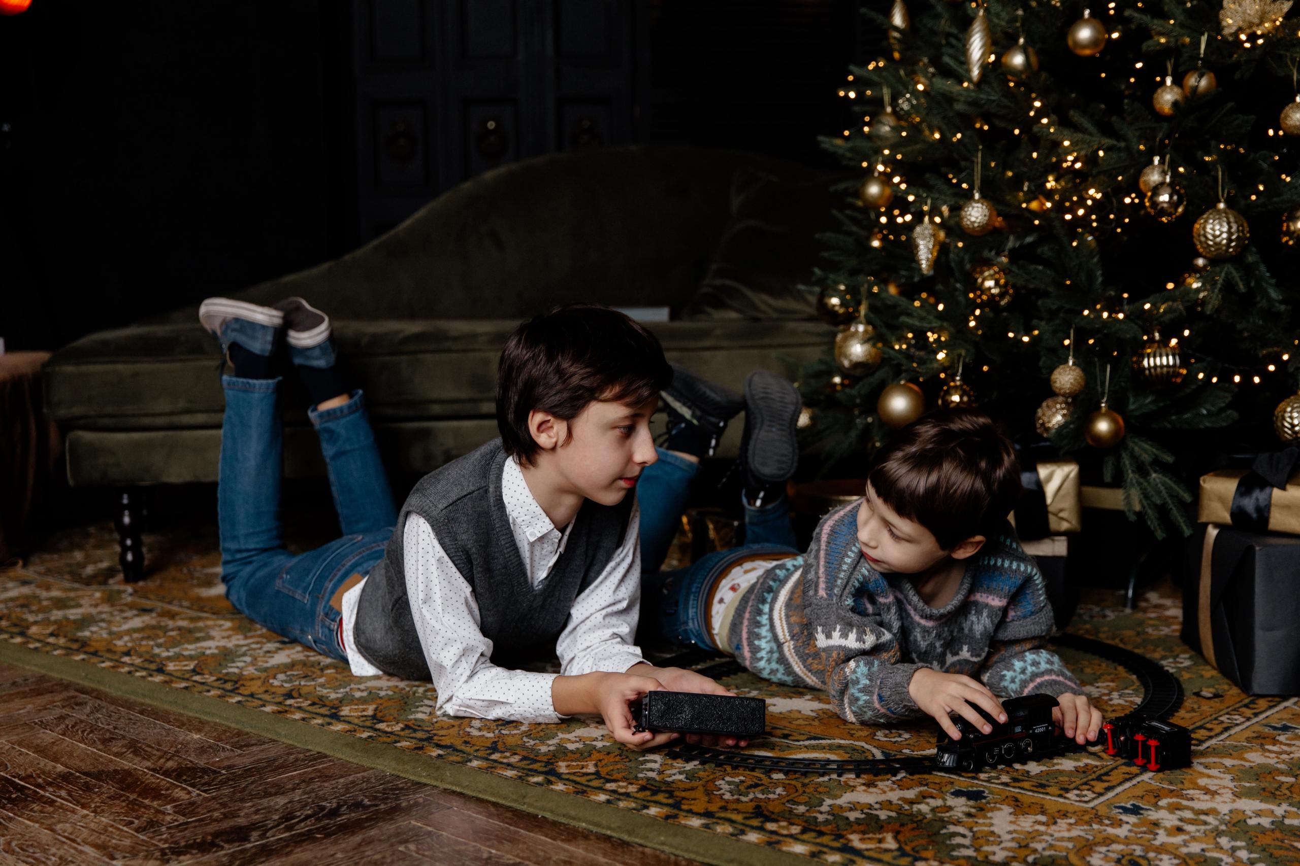 dos chicos leen un libro tirados frente al arbol de navidad
