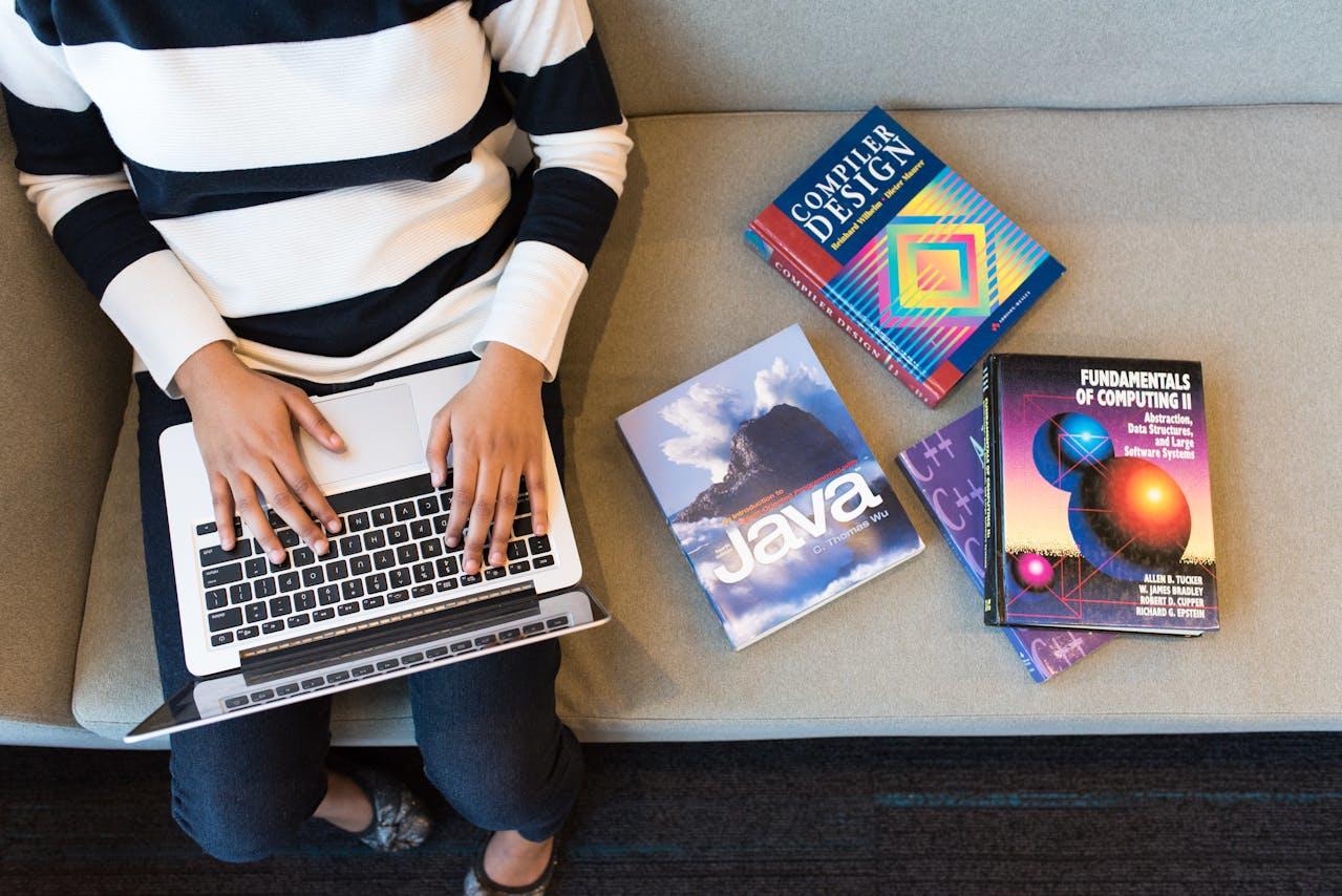 persona con computadora y libros de texto sobre lenguajes de programacion
