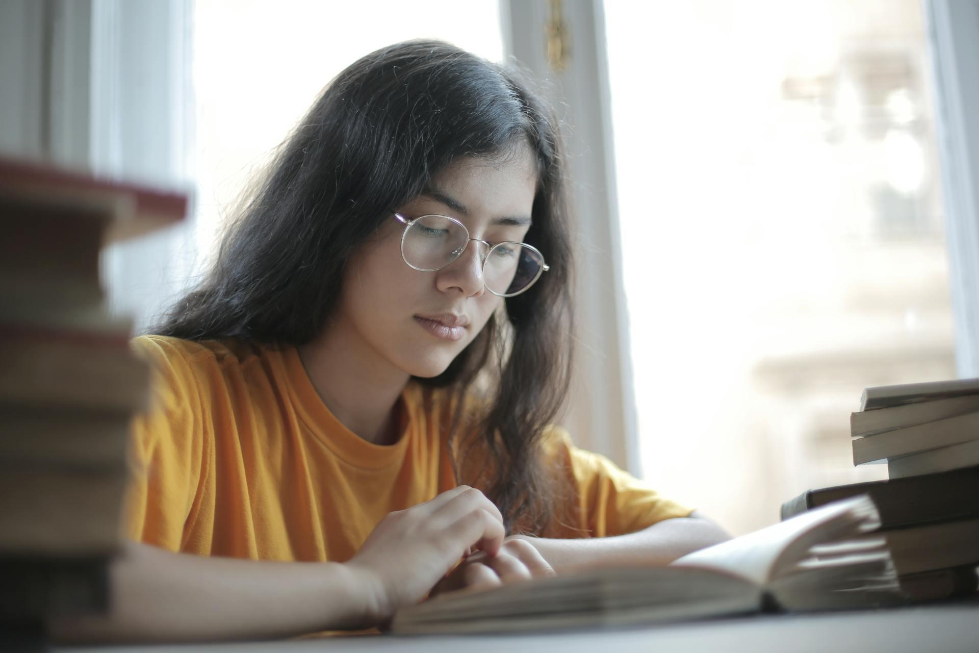 Mujer con anteojos sentada en el escritorio con libros.