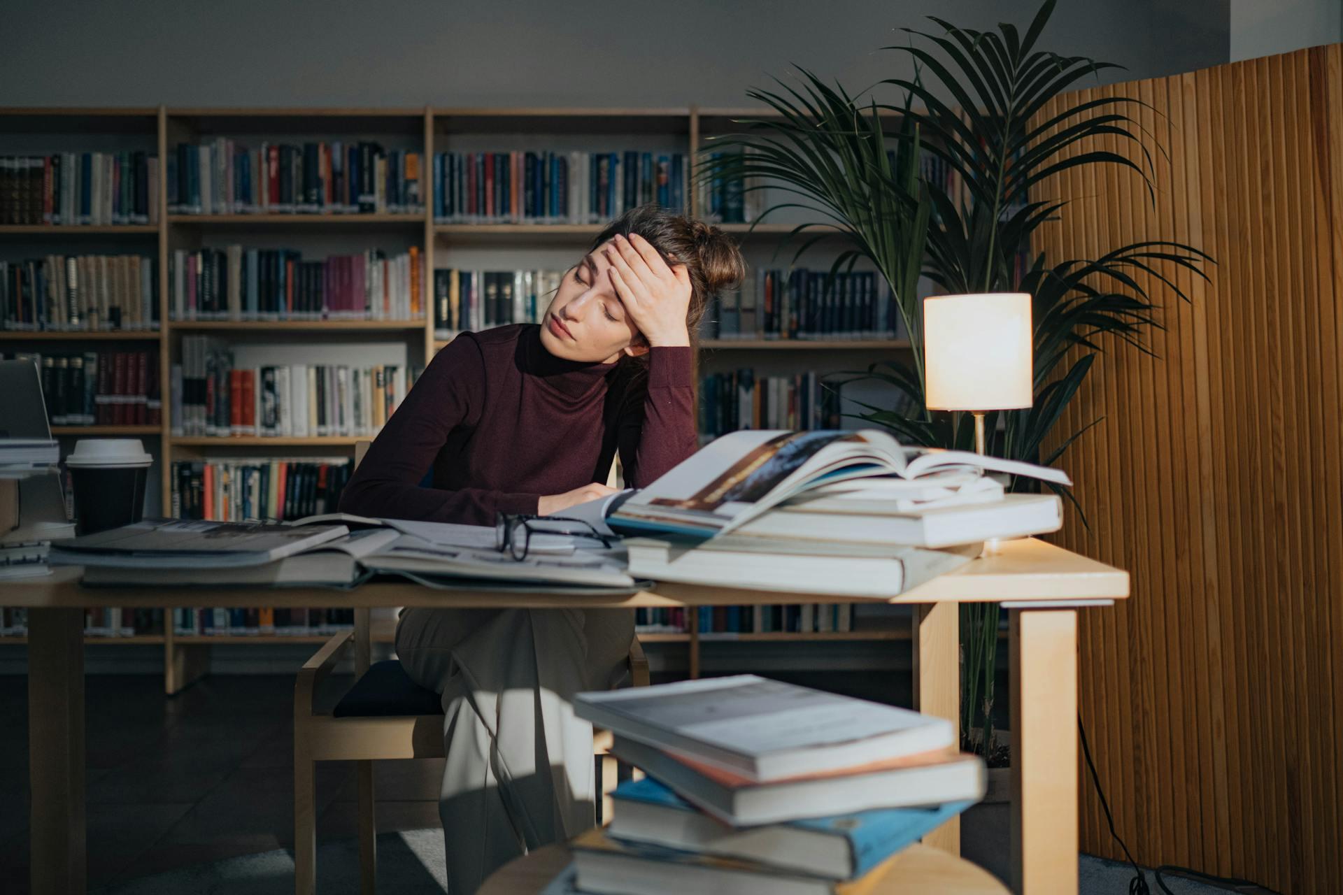 Mujer sentada en el escritorio con libros y atrás una biblioteca.