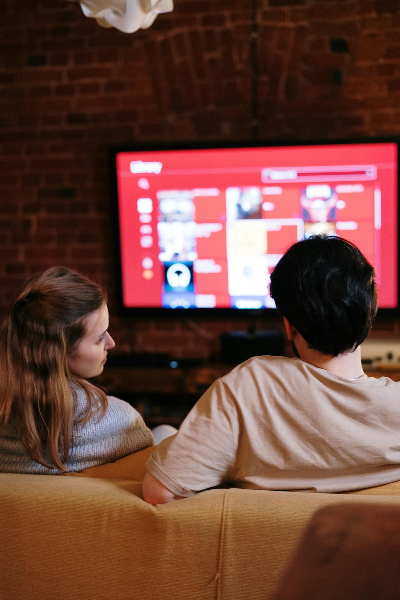 Hombre y mujer de espaldas frente a la tv prendida.