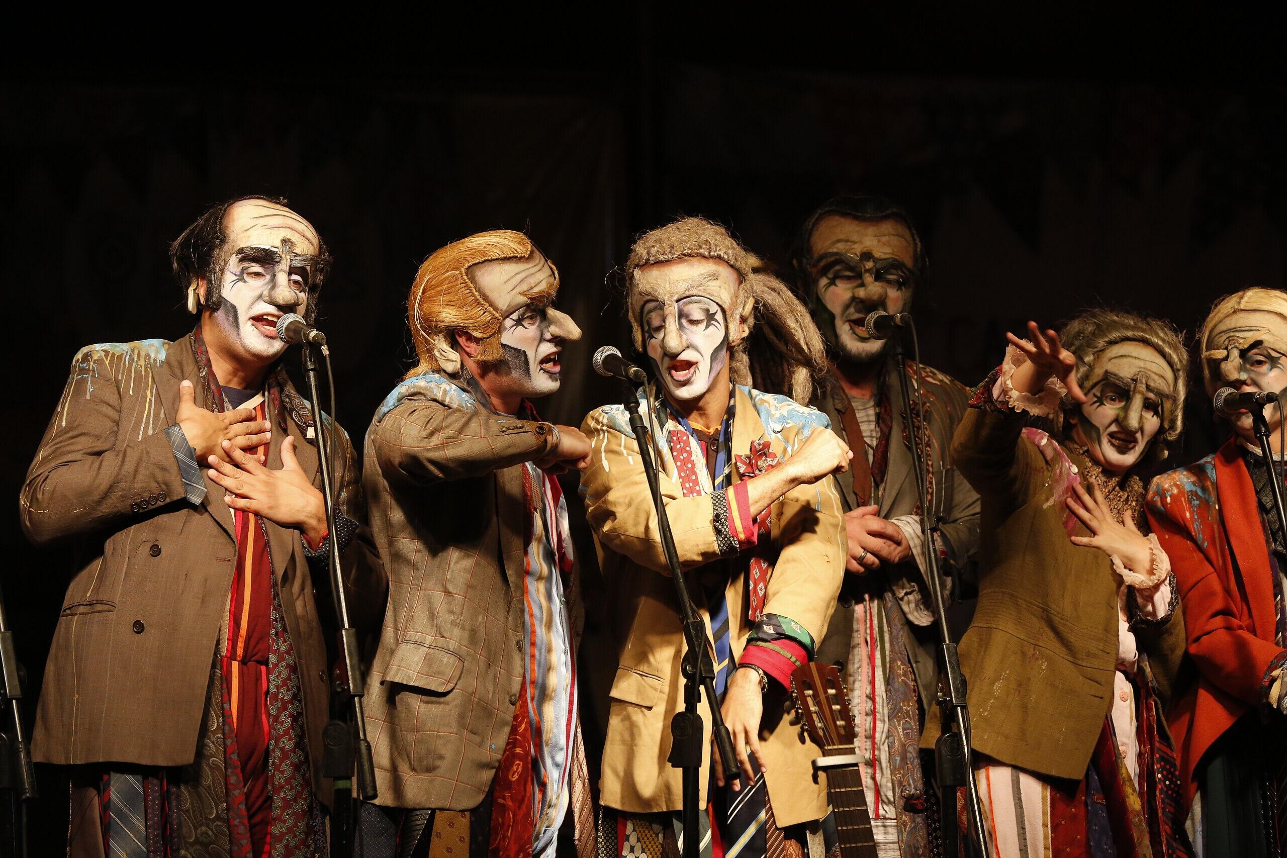  personas sobre un escenario frente a micrófonos cantando disfrazadas