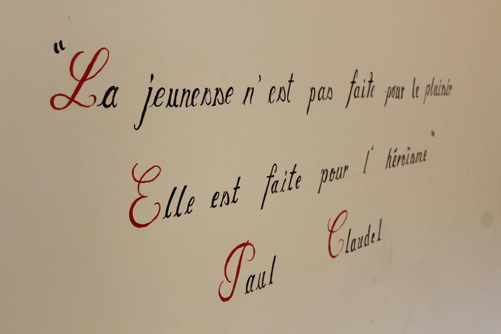 En una pared blanca está inscrita la frase: "la jeunesse n'est pas faite pour le plaisir, elle est faite pour l'heroïsme" Paul Claudel