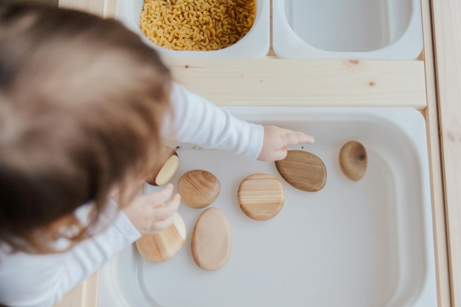 Vista superior de un niño jugando con discos de madera en una mesa sensorial de aprendizaje. Foto de Tatiana Syrikova.
