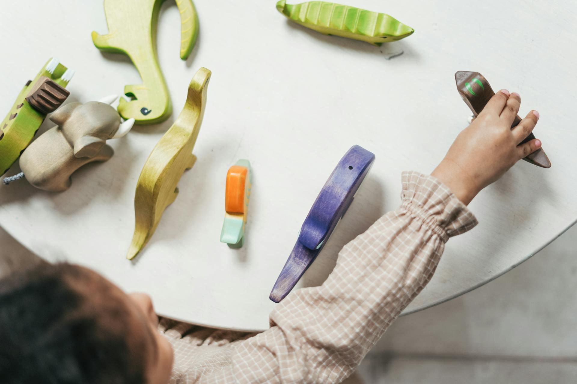 Vista cenital de las manos de un niño pequeño jugando con materiales sensoriales de madera con formas de animales. Foto de cottonbro studio.