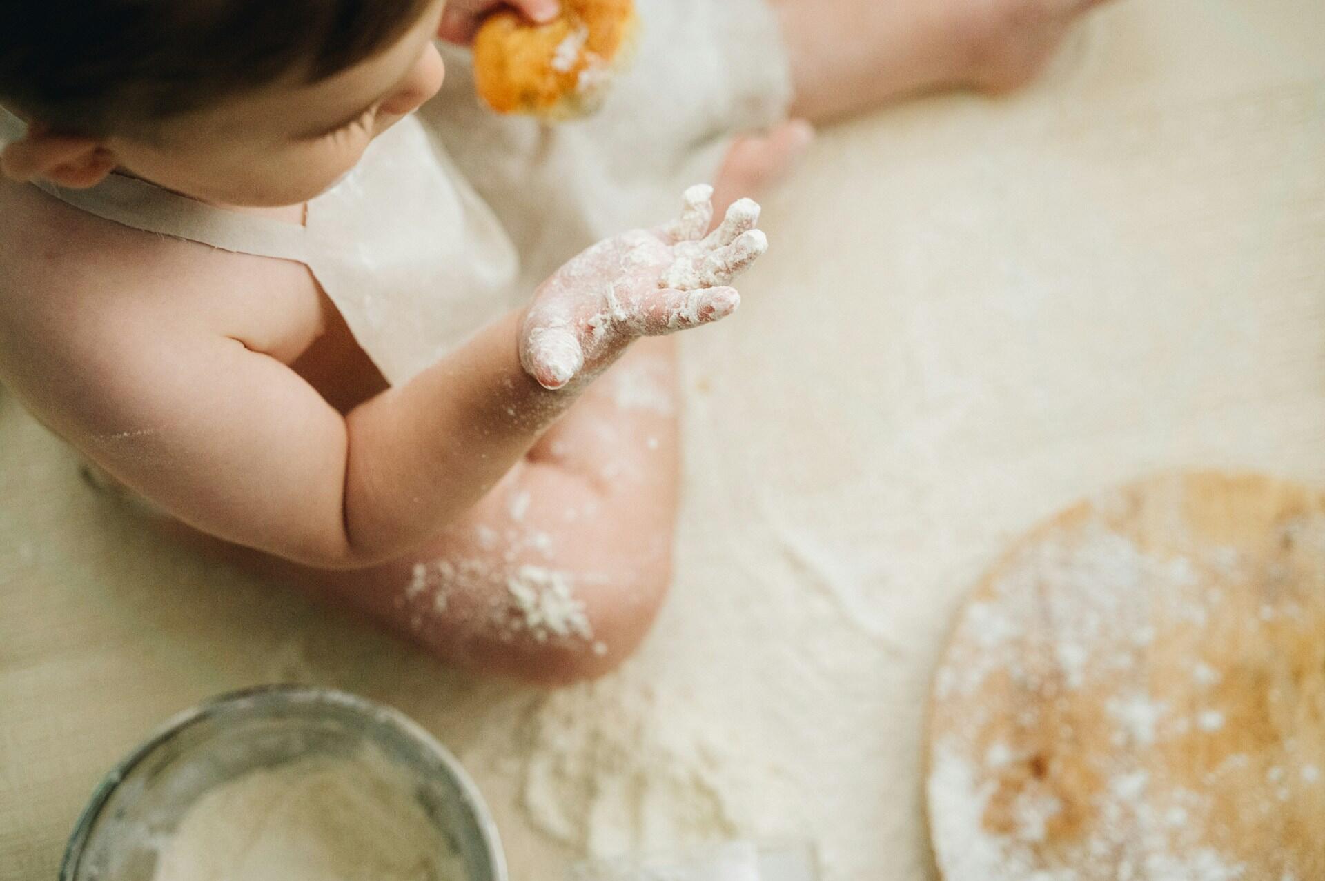 Primer plano de la mano de un niño pequeño cubierta de harina mientras participa en la cocina. Foto de serjan midili.