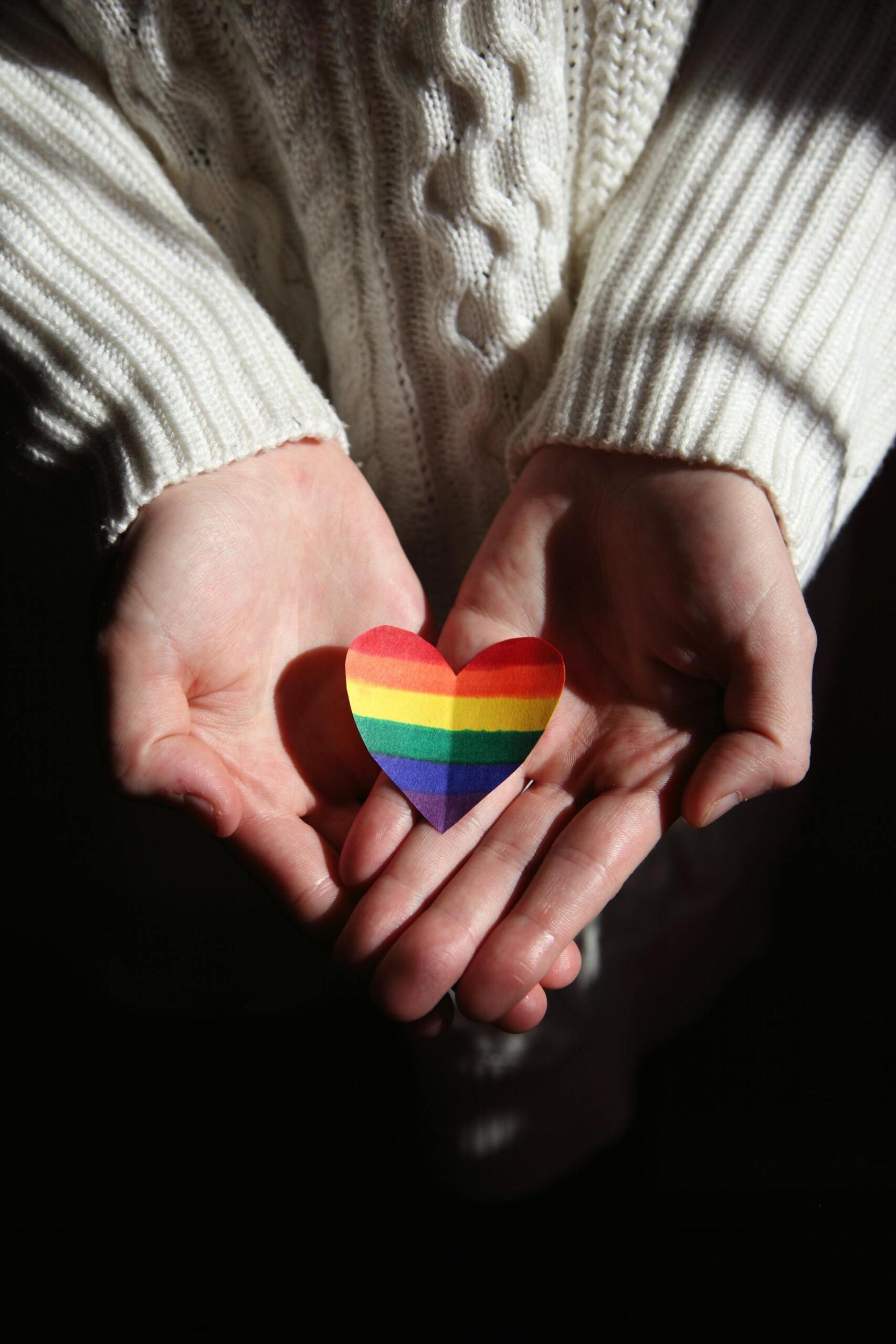 Manos de una persona sosteniendo un corazón de papel con los colores del arcoíris, representando el matrimonio igualitario y los derechos LGBT. Fotógrafo: Alexander Grey.