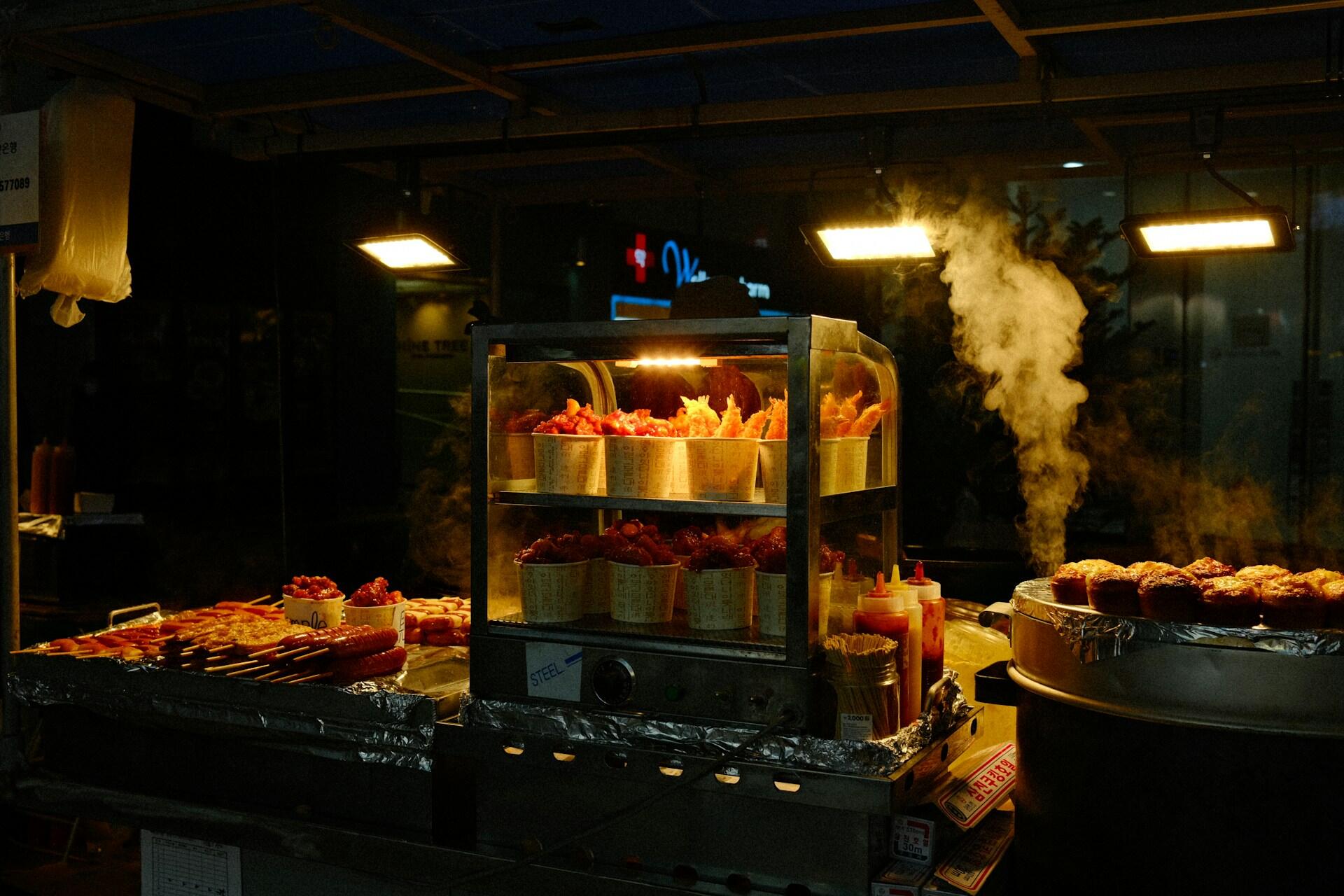 El vapor se eleva desde un puesto en Myeongdong, el epicentro de la comida callejera en Seúl. Al caer la noche, estas vitrinas iluminadas se convierten en un espectáculo de sabores y olores, ofreciendo delicias a locales y turistas. Fuente: Varta Matsakian