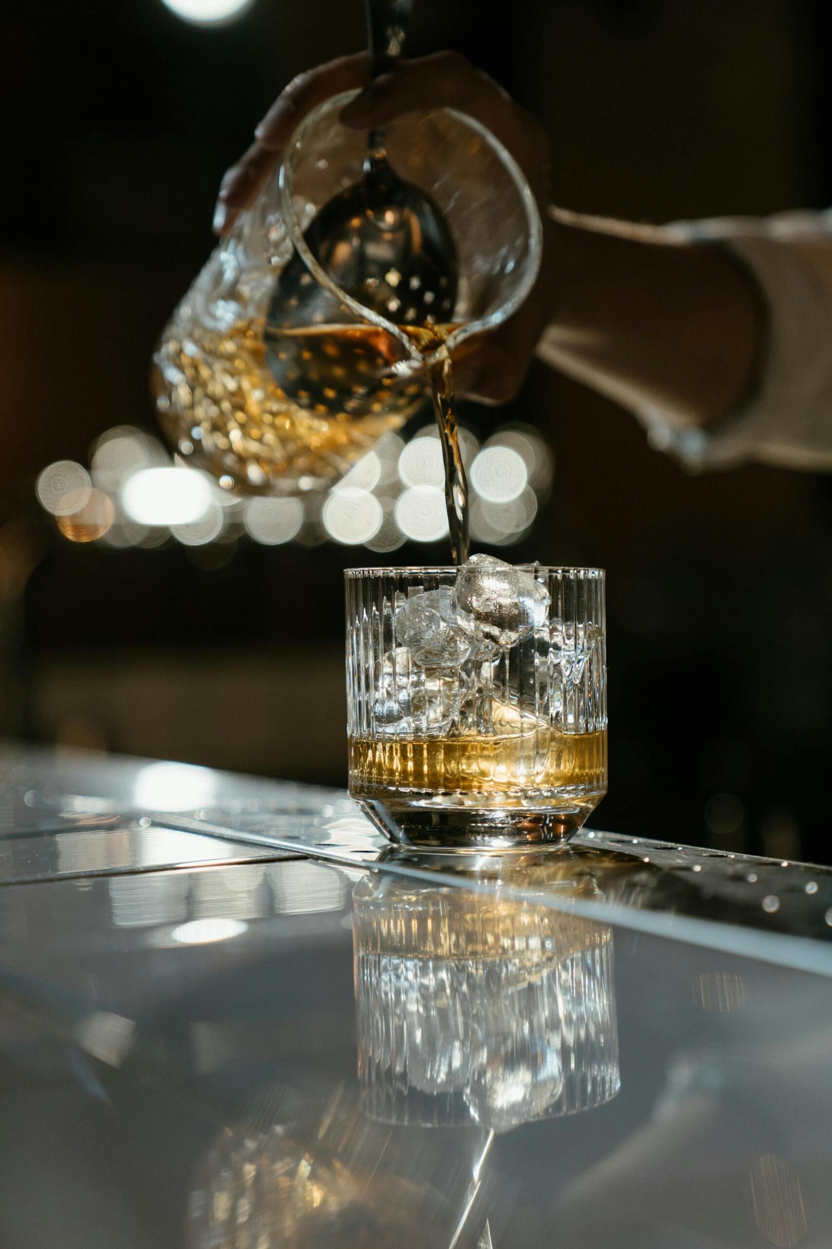 Barra de un bar. Whisky sirviéndose en un vaso con hielo desde una coctelera, ilustrando el alto consumo de esta bebida en Uruguay. Fuente: cottonbro studio.