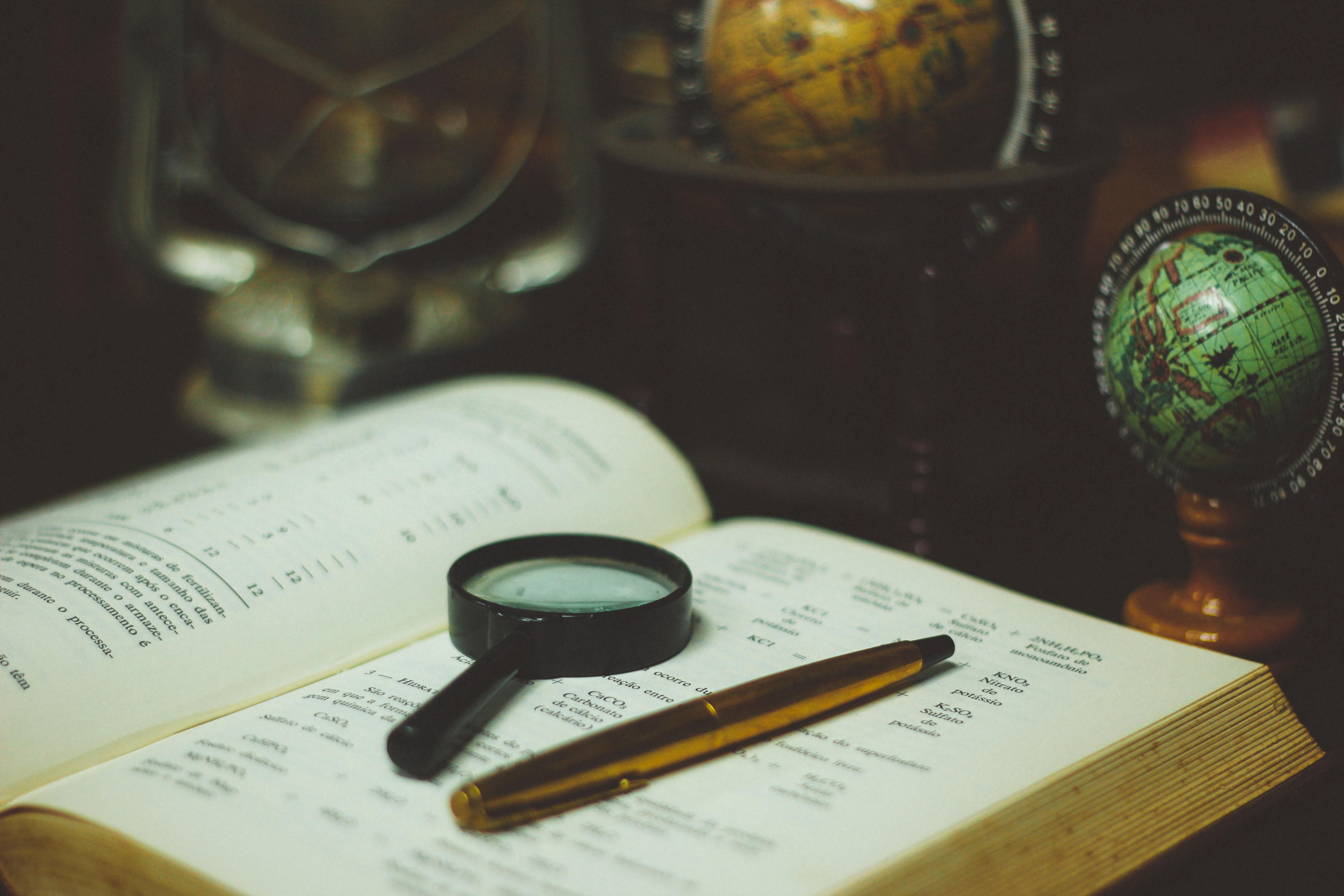 pen, magnifying glass, open book and globe
