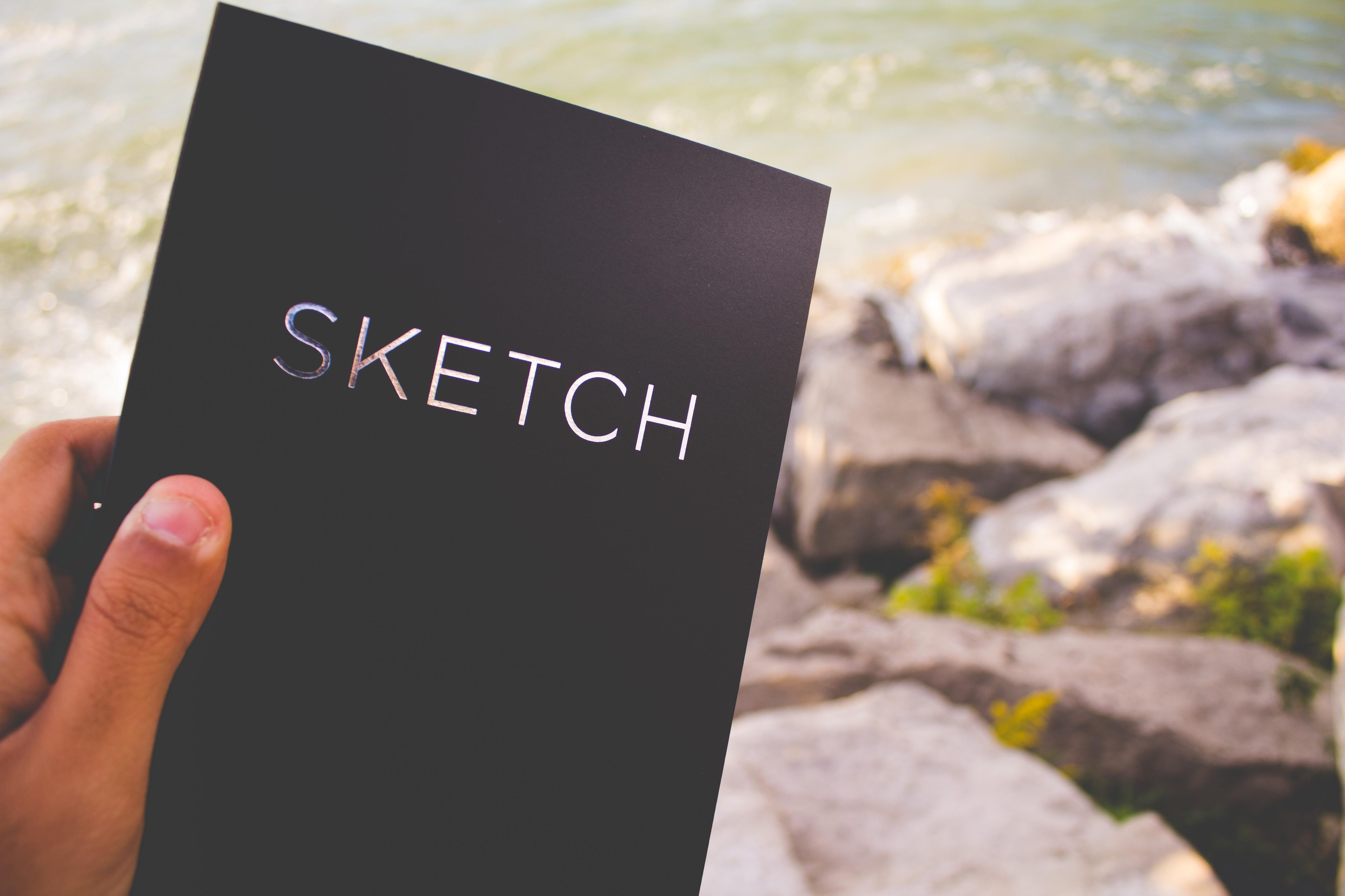 person holding sketch book at the beach