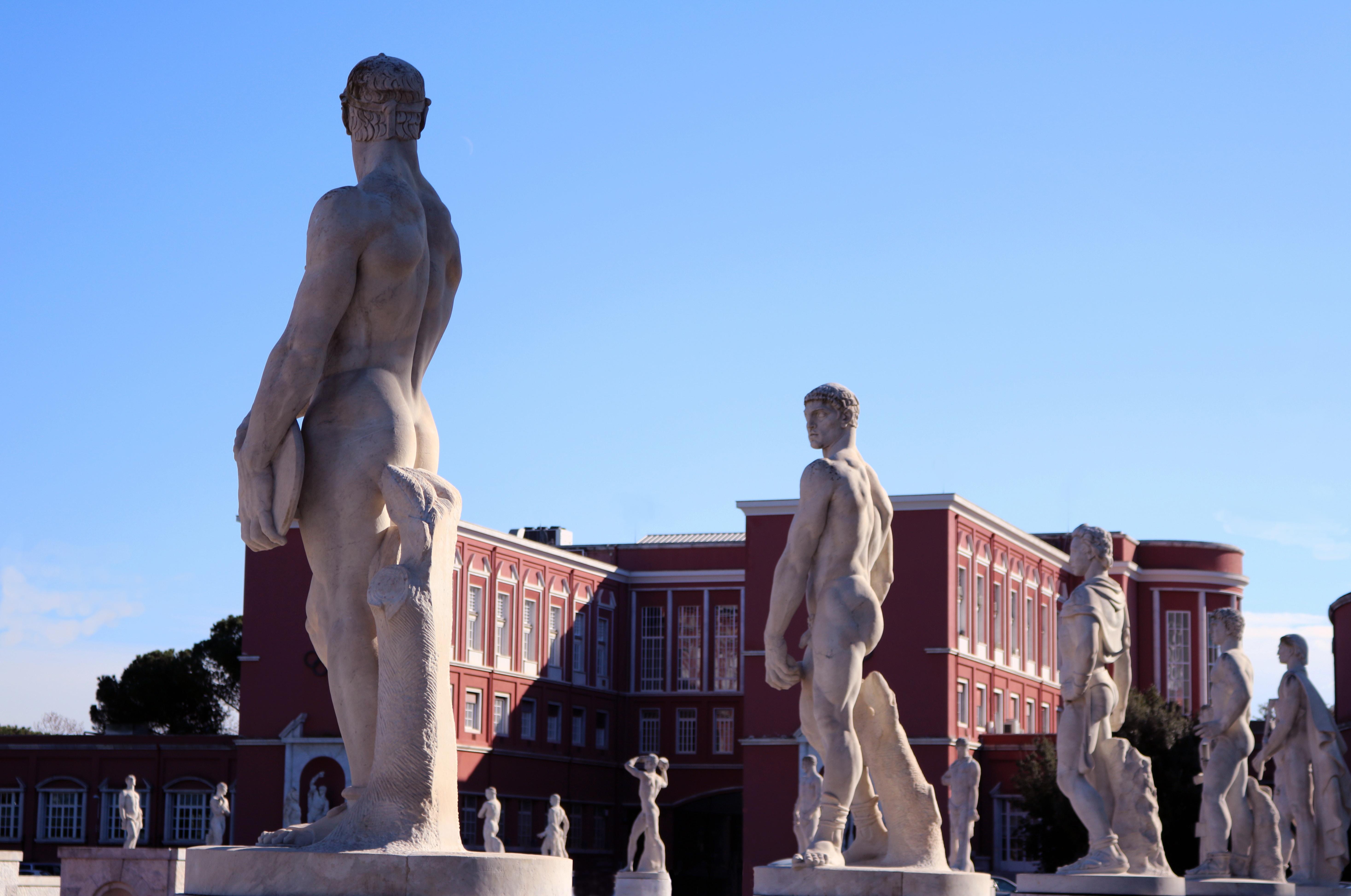 statues of men showing human anatomy near brown building during daytime